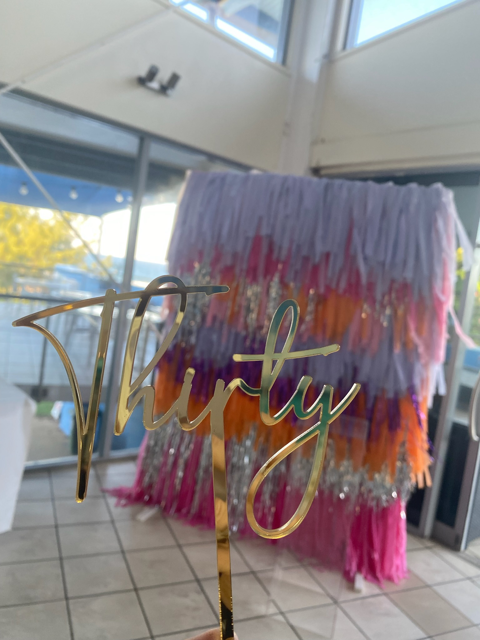 Close-up of a gold 'Thirty' cake topper with a colorful, fringed cake in the background for a 30th birthday celebration.