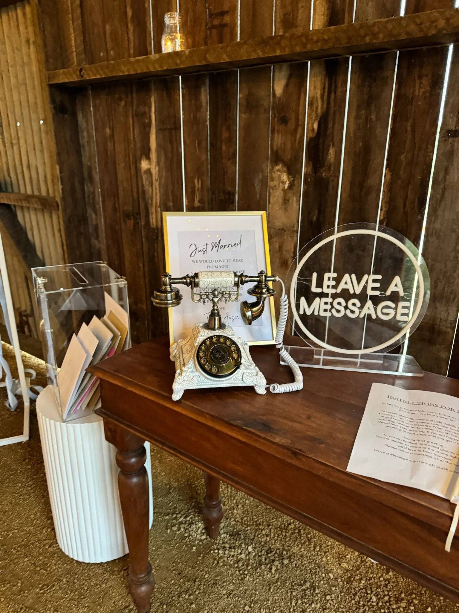Table with vintage rotary phone, sign that says 'Leave a Message,' framed note about just married, and info sheet, against a wooden wall with a small jar on top.