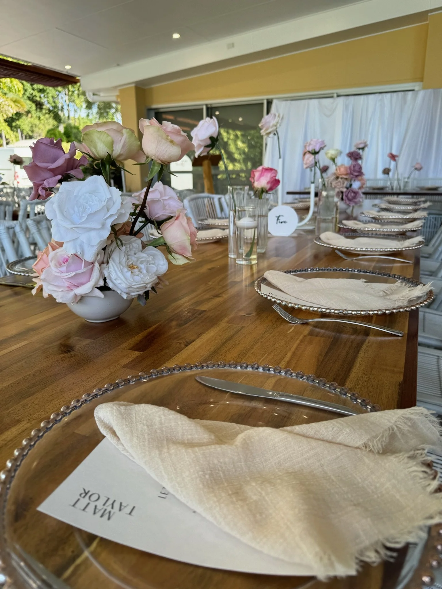 A beautifully decorated table set for a special occasion with floral centerpieces, place settings with cream-colored cloth napkins, and glass plates.