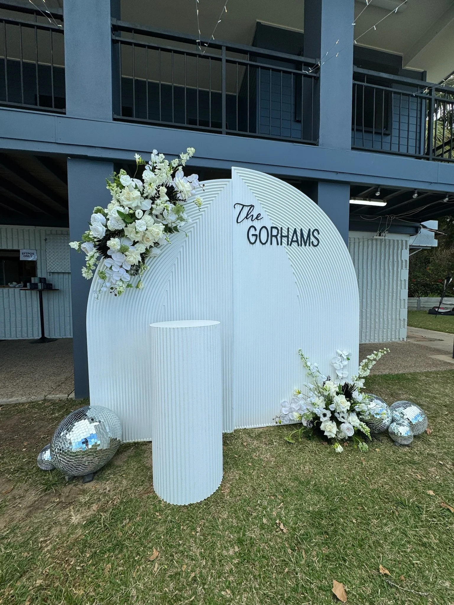 Decorative outdoor display with a white backdrop, floral arrangements, large mirrored disco balls, and the sign 'The Gorhams' for a celebration or event.