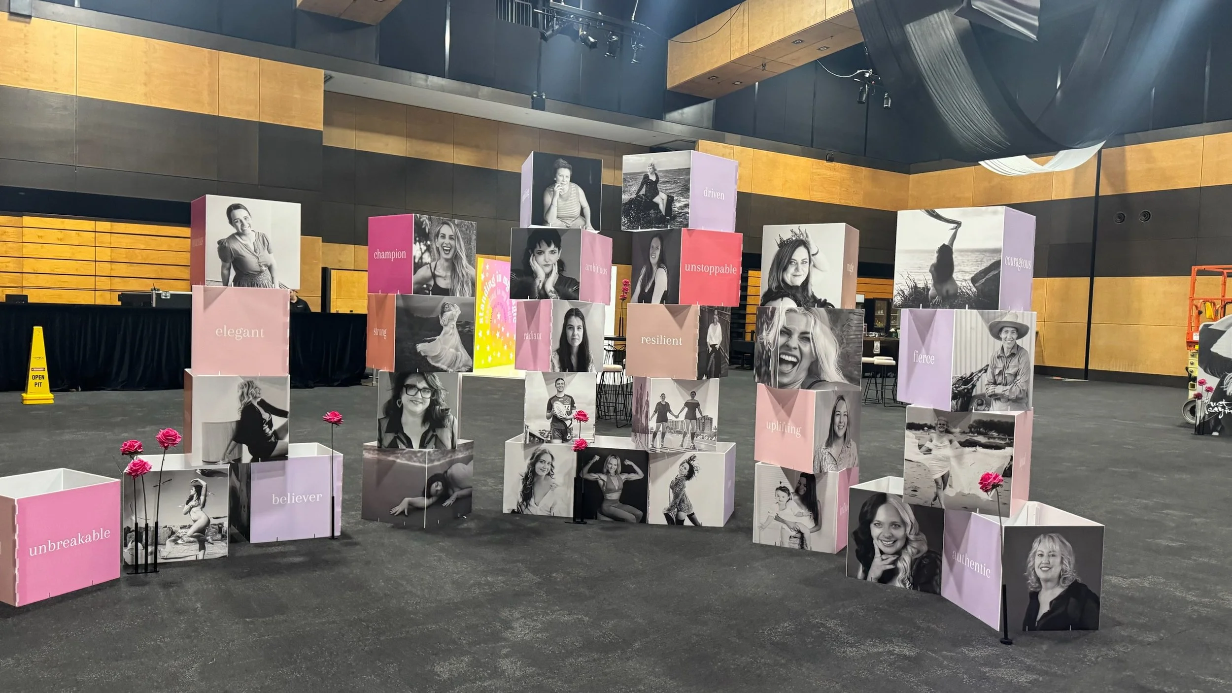 An indoor display of decorated cubes featuring black-and-white photos of women with words like 'champion,' 'resilient,' 'fierce,' and 'unbreakable,' along with pink flowers in small pots.