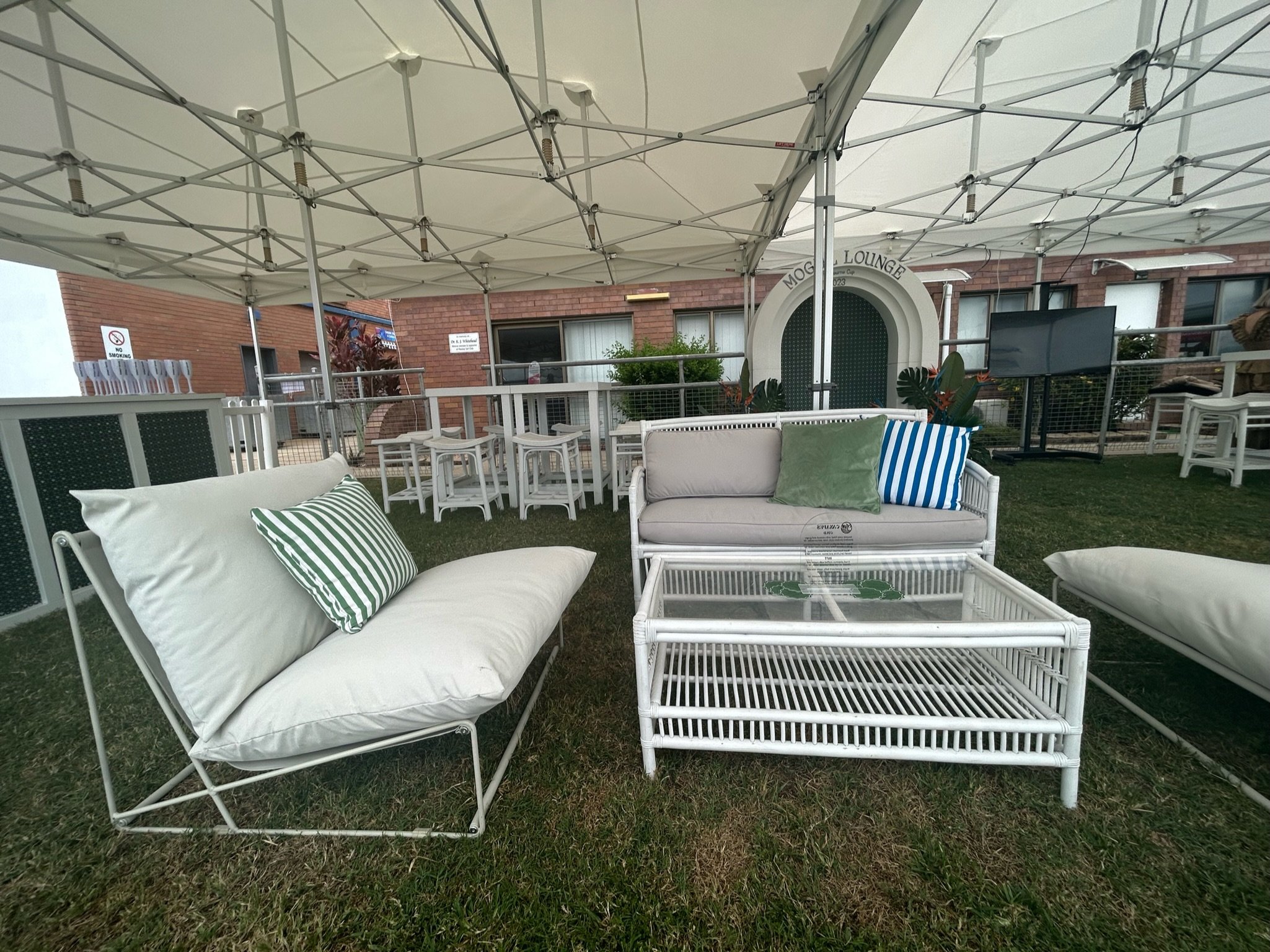 Outdoor seating area with white wicker furniture, cushions, and a canopy at a hotel or lounge.