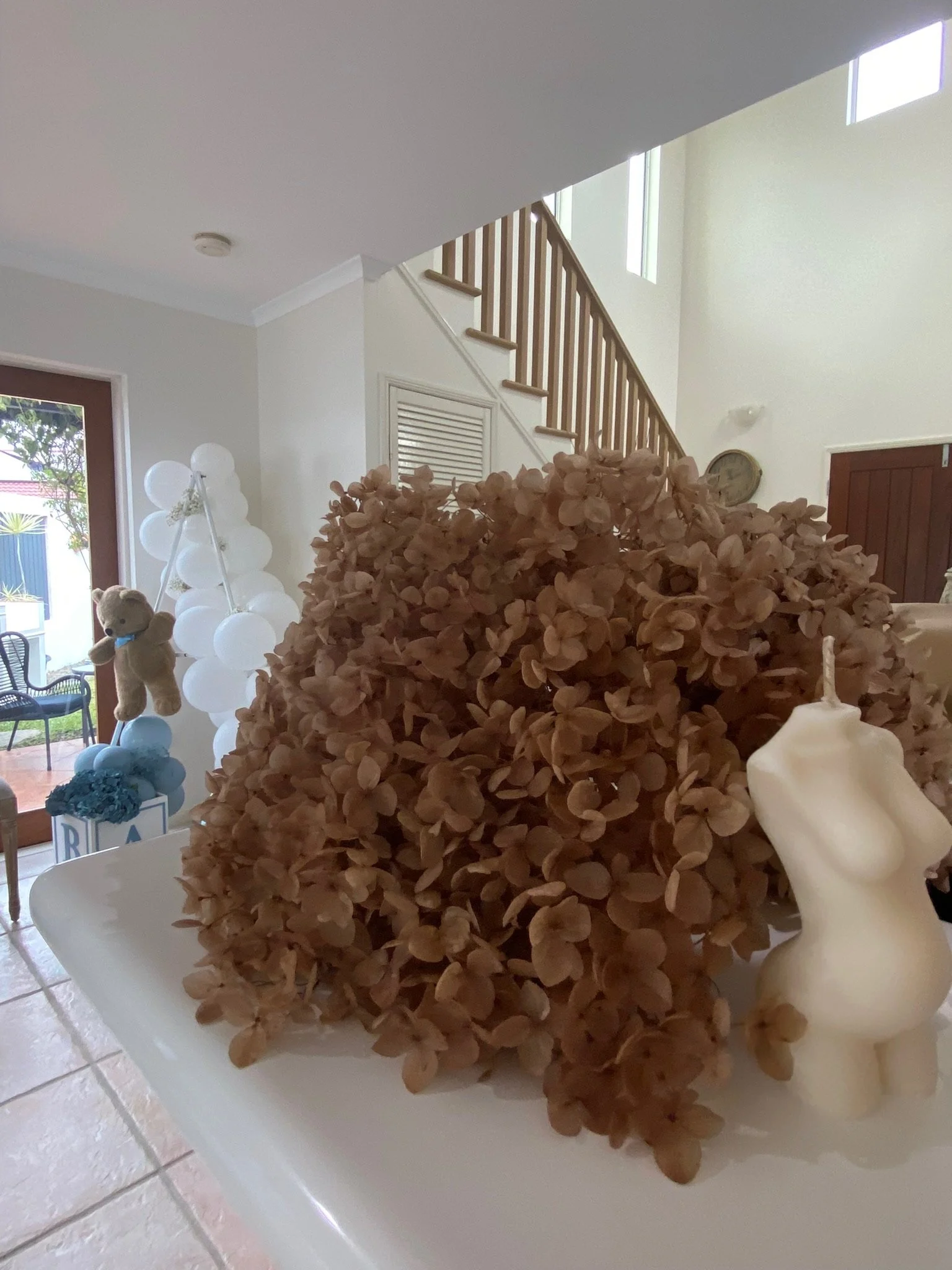 Decorative display with dried brown hydrangea flowers and a white rabbit-shaped candle on a table in a bright, modern living room.
