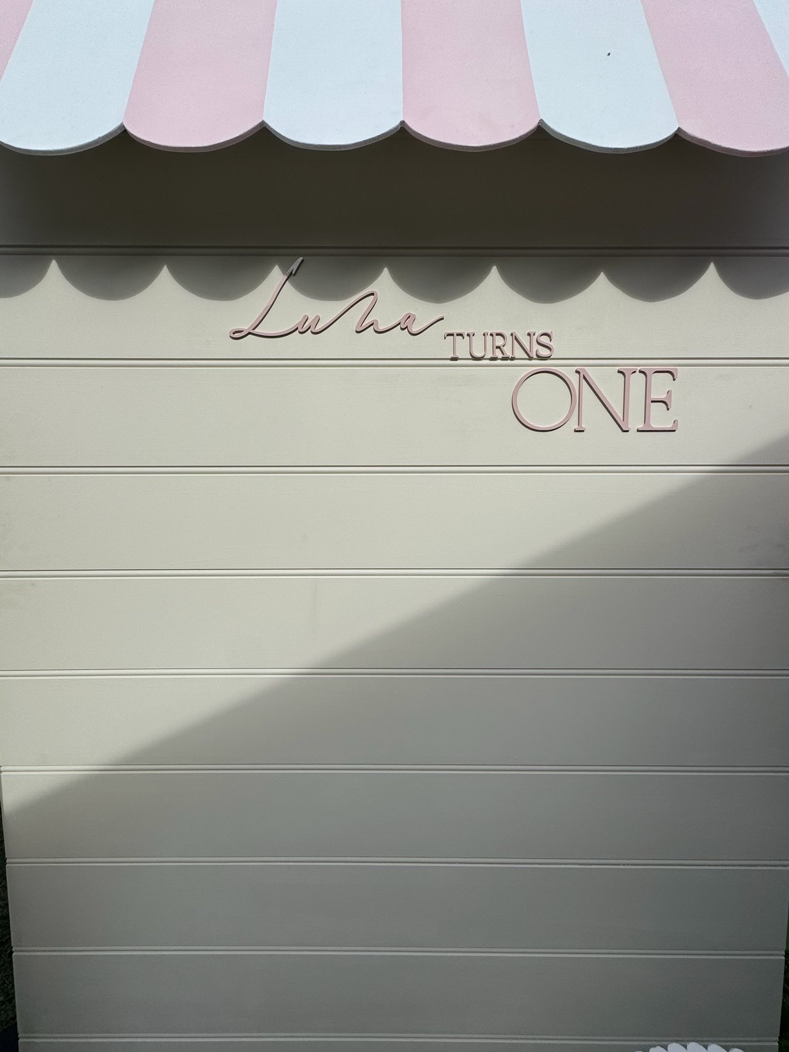 Decorative wall with pink and blue scalloped awning and the words 'Luha turns one' in pink and purple lettering.