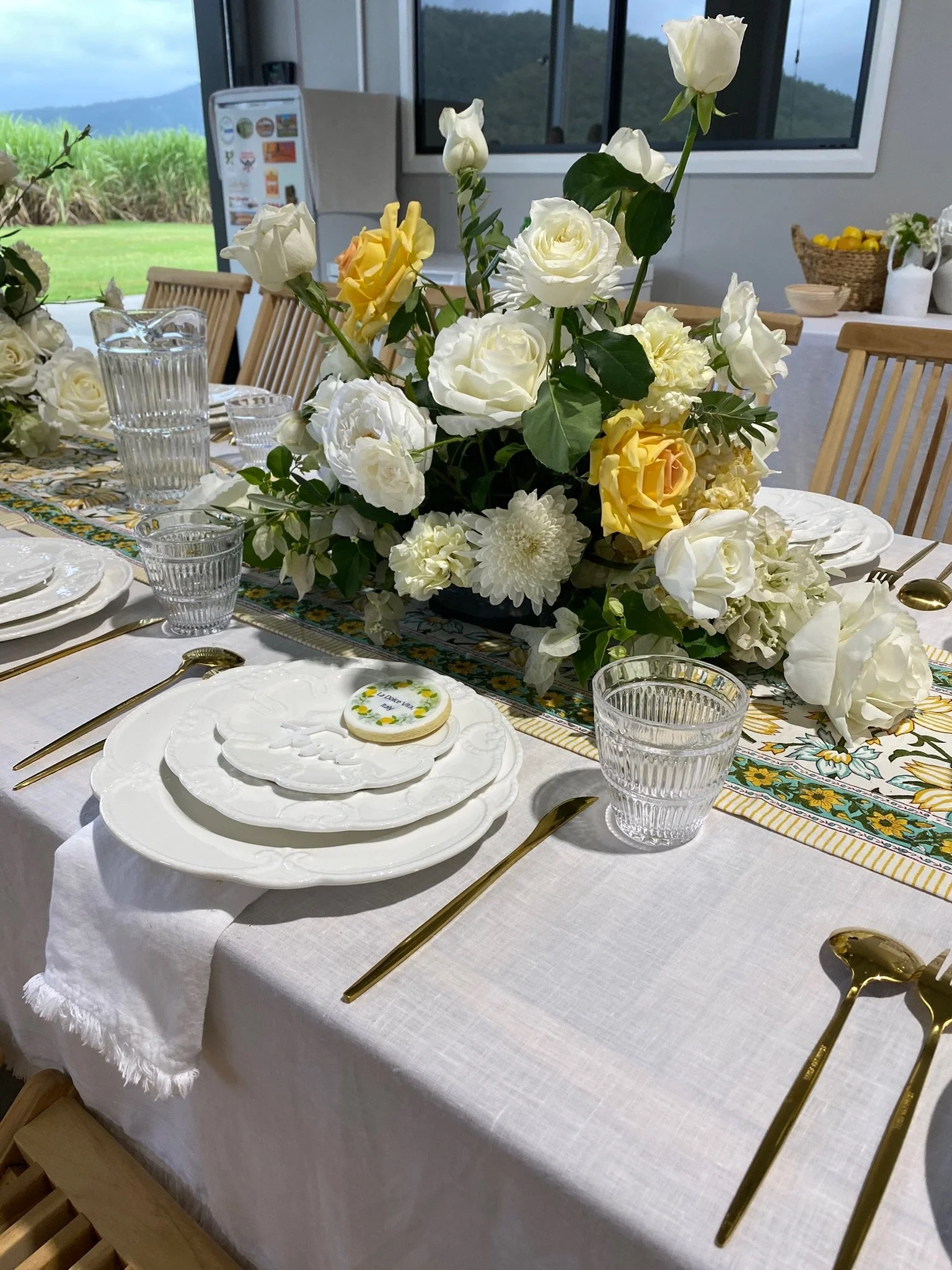 A decorated dining table with a floral centerpiece, white plates, gold utensils, and glassware set for a meal.