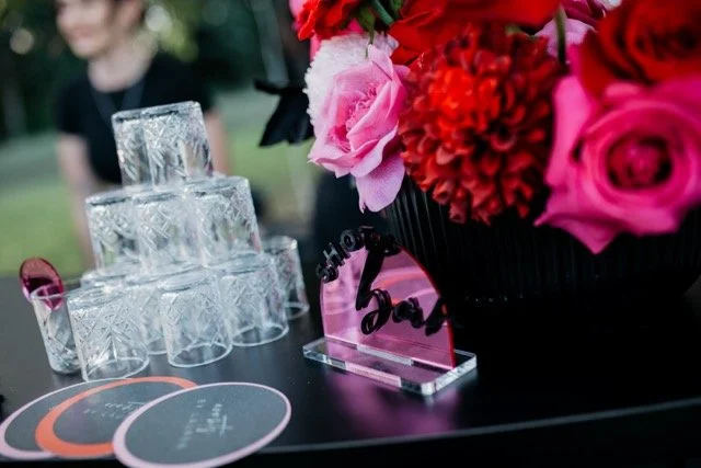A table with a bouquet of pink and red flowers, glass jars stacked in a pyramid, and a sign that reads 'love'.