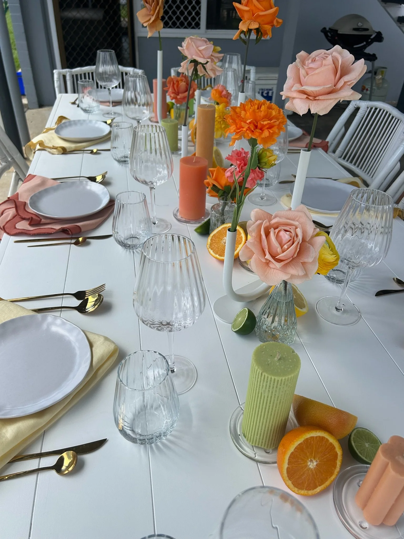 Decorated outdoor dining table with floral centerpieces, candles, and glassware, set for a meal.
