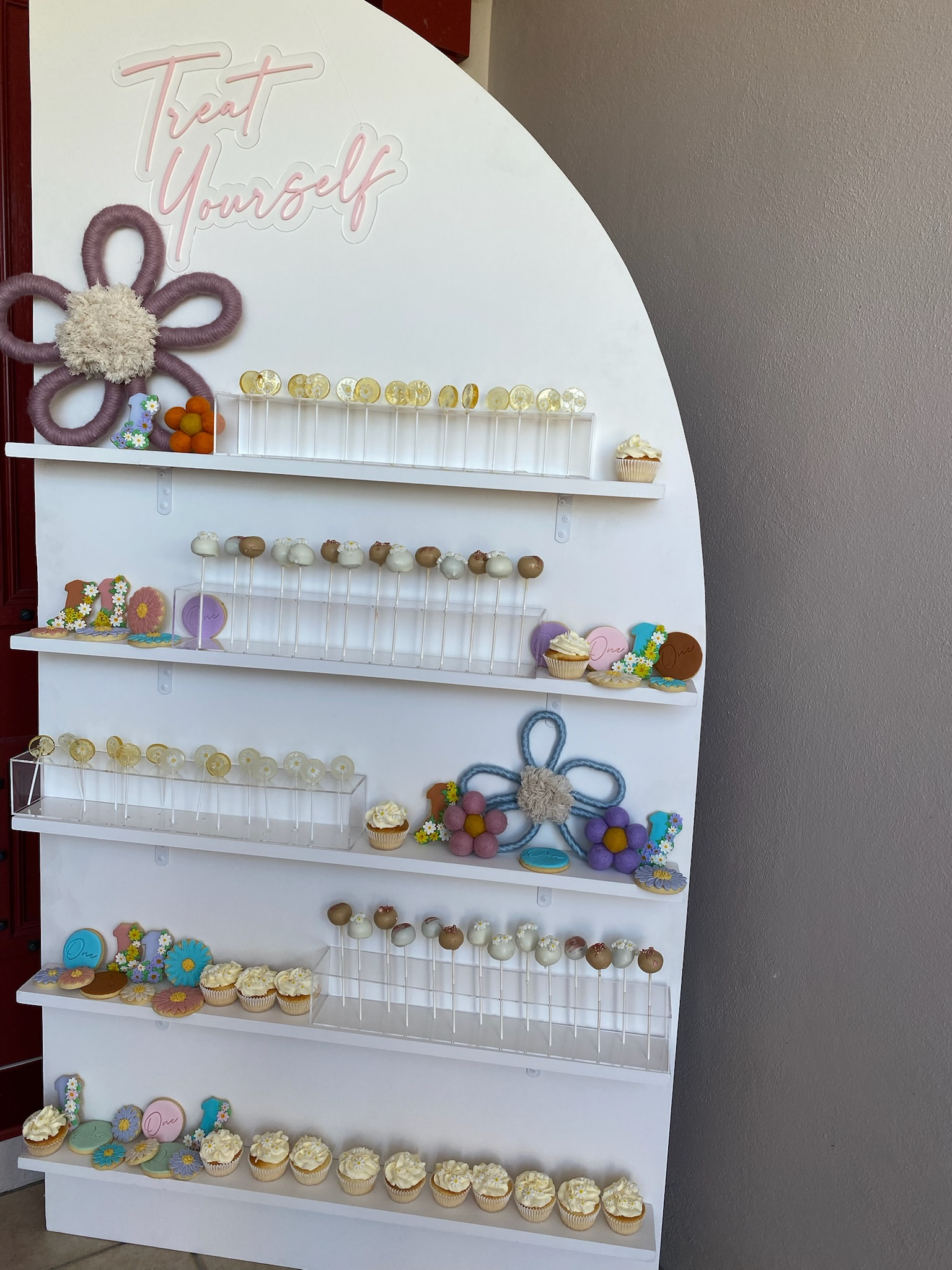 Display board with the words "Treat Yourself" at the top, decorated with flower and cupcake themed embellishments, showcasing cupcakes and decorative items.