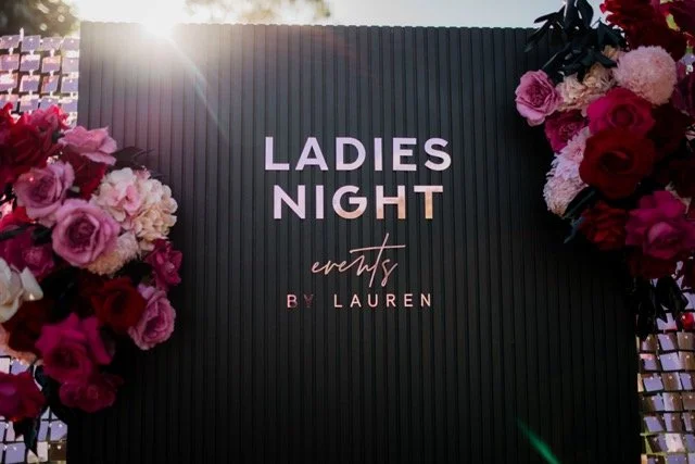 Black vertical sign board with pink, purple, and red flowers on both sides, reading 'Ladies Night events by Lauren'.