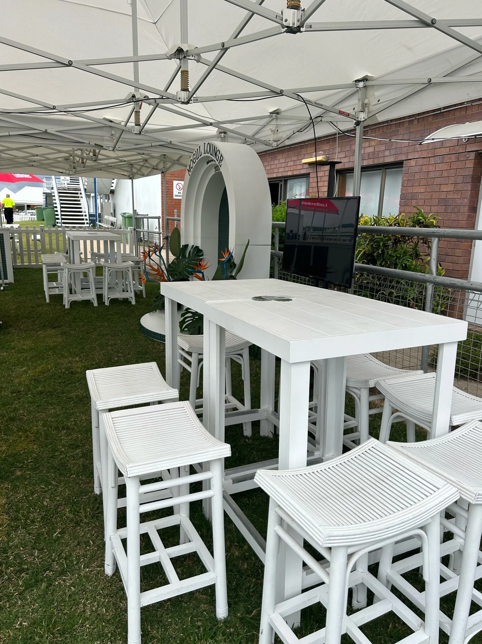 Outdoor seating area with white tables and chairs under a large white canopy. A decorative structure labeled 'Vogul Lounge' is also visible.