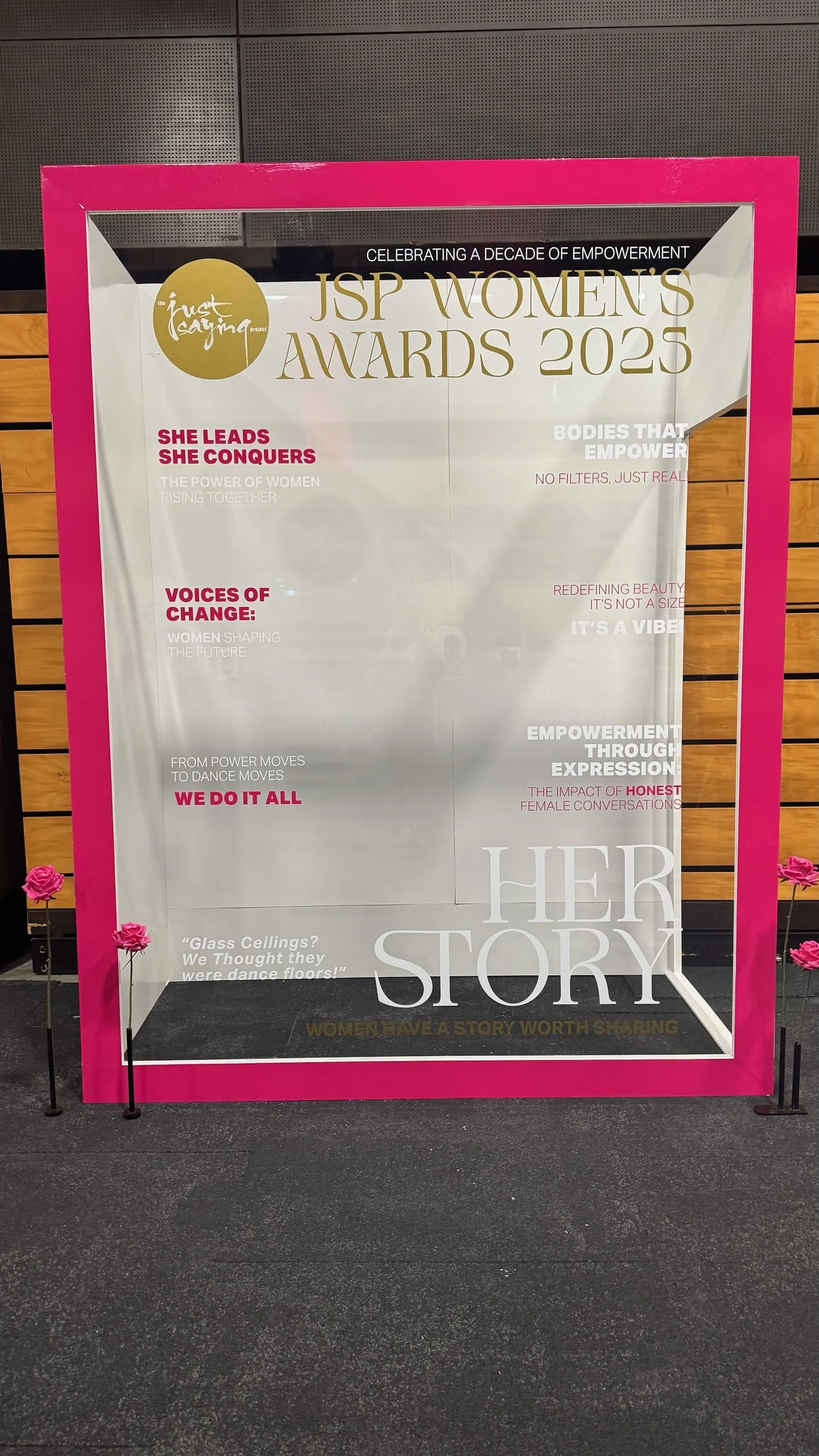 A glass display case celebrating the JSP Women's Awards 2023 with various textual elements and pink flowers outside.