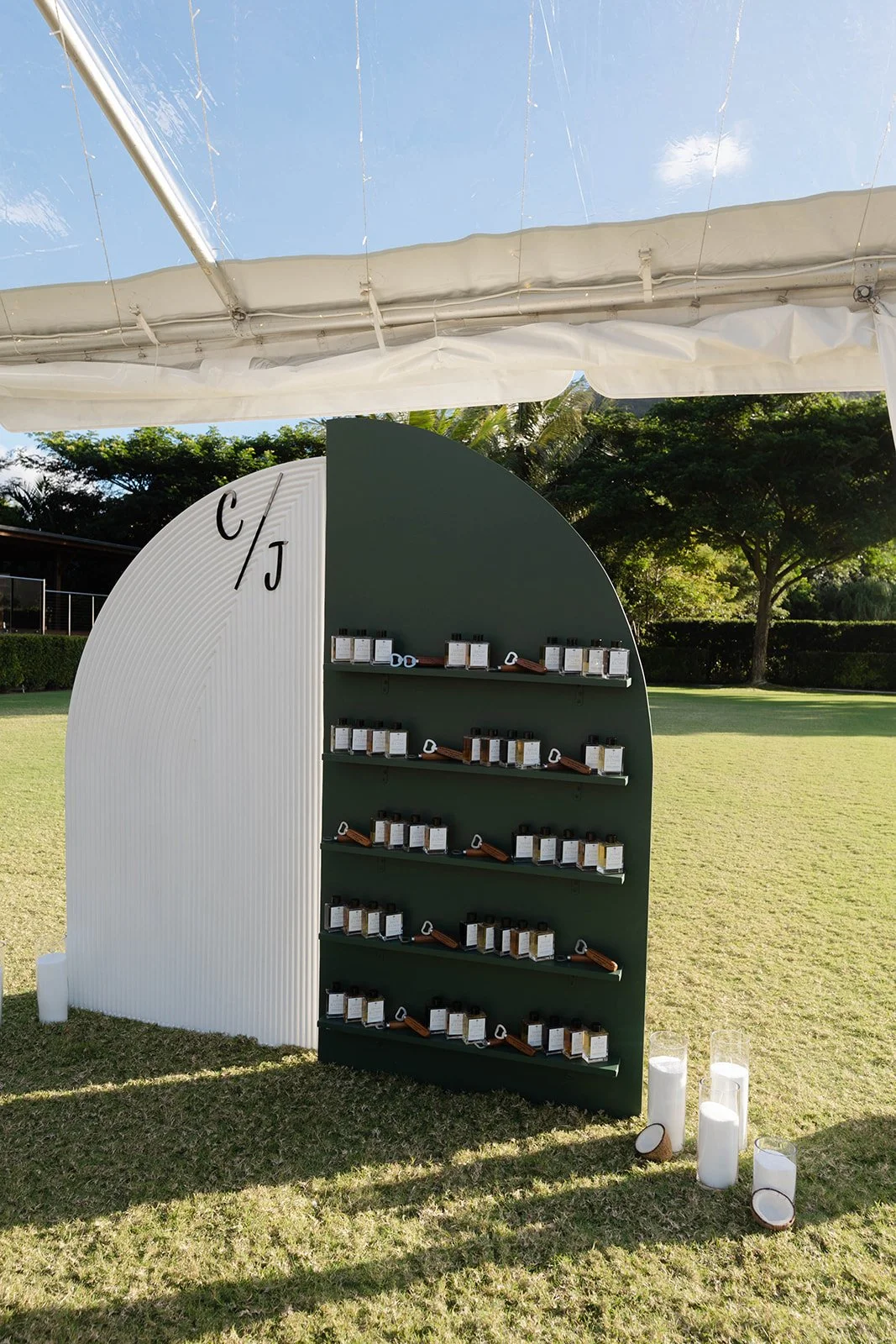 Display stand with multiple bottles arranged on shelves, set outdoors on grass under a tent