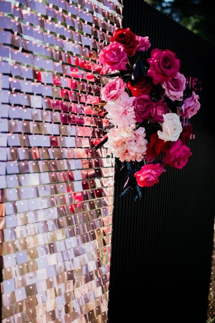 Bouquet of pink, red, and white roses and carnations on a shiny, reflective surface with a black background.
