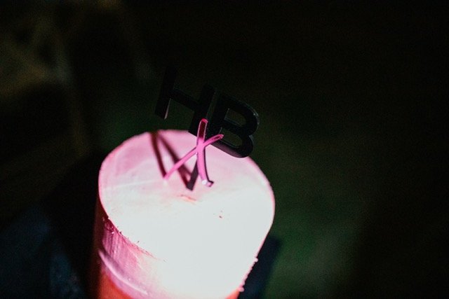 A birthday cake with pink frosting and a black 'HBD' candle on top.