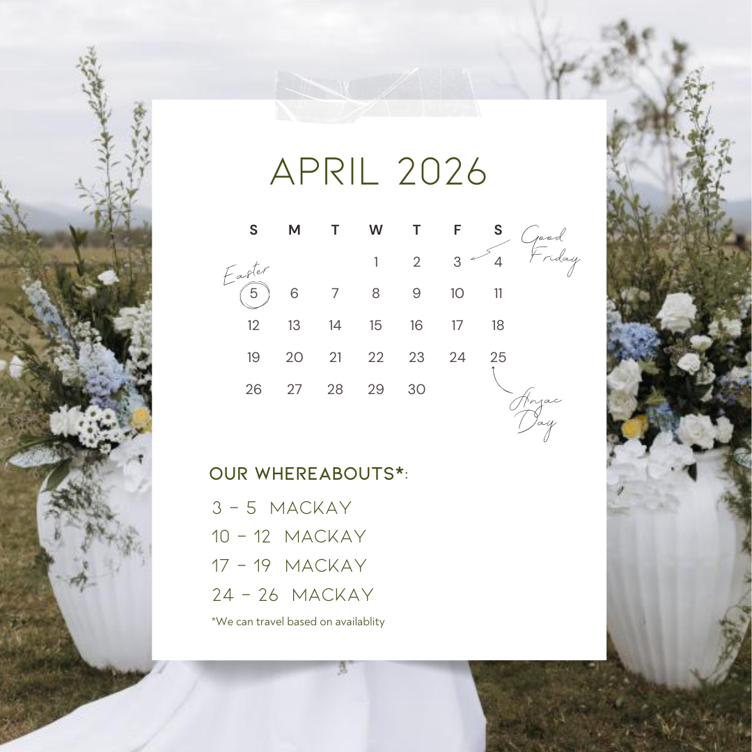April 2026 calendar overlay on a floral outdoor arrangement with white and blue flowers, hints of greenery, and a blurred natural landscape in the background.