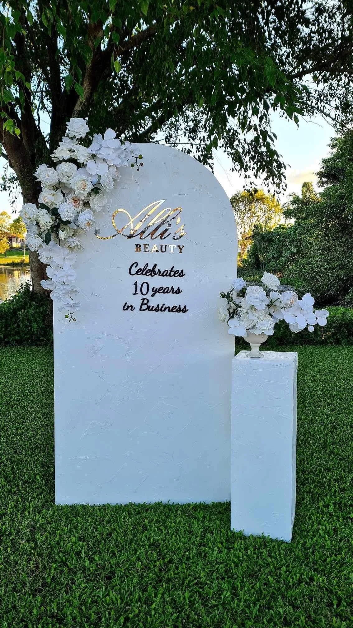 A white outdoor display board decorated with white flowers, celebrating Ali's 10 years in business.