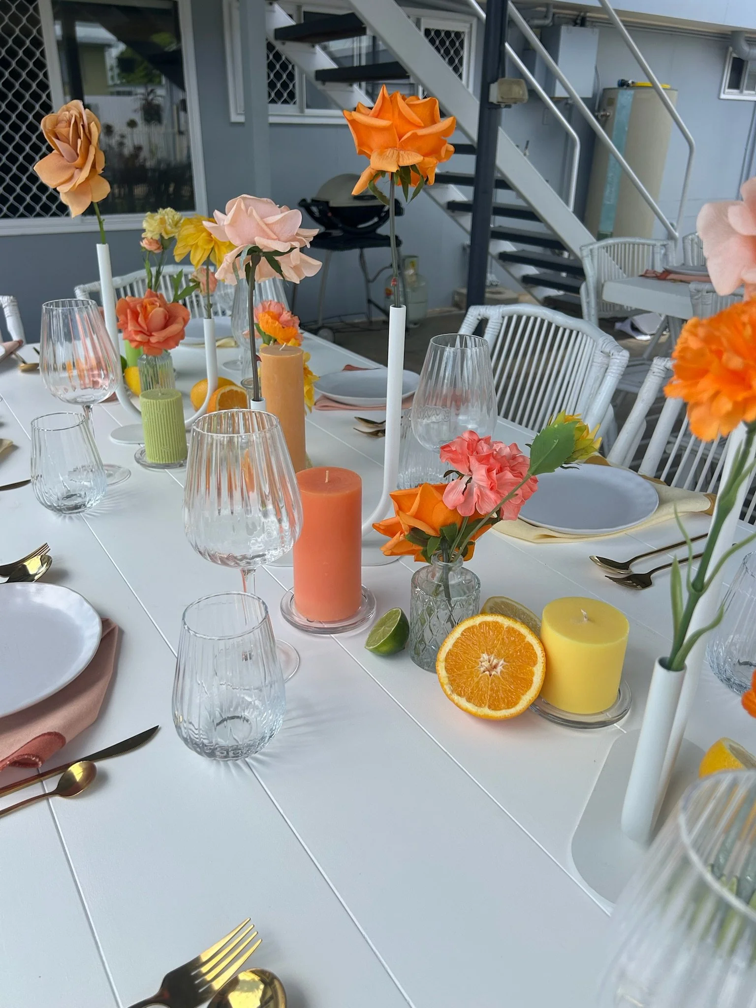 Decorative outdoor dining table with colorful flowers, candles, glassware, plates, and utensils, set for a gathering.