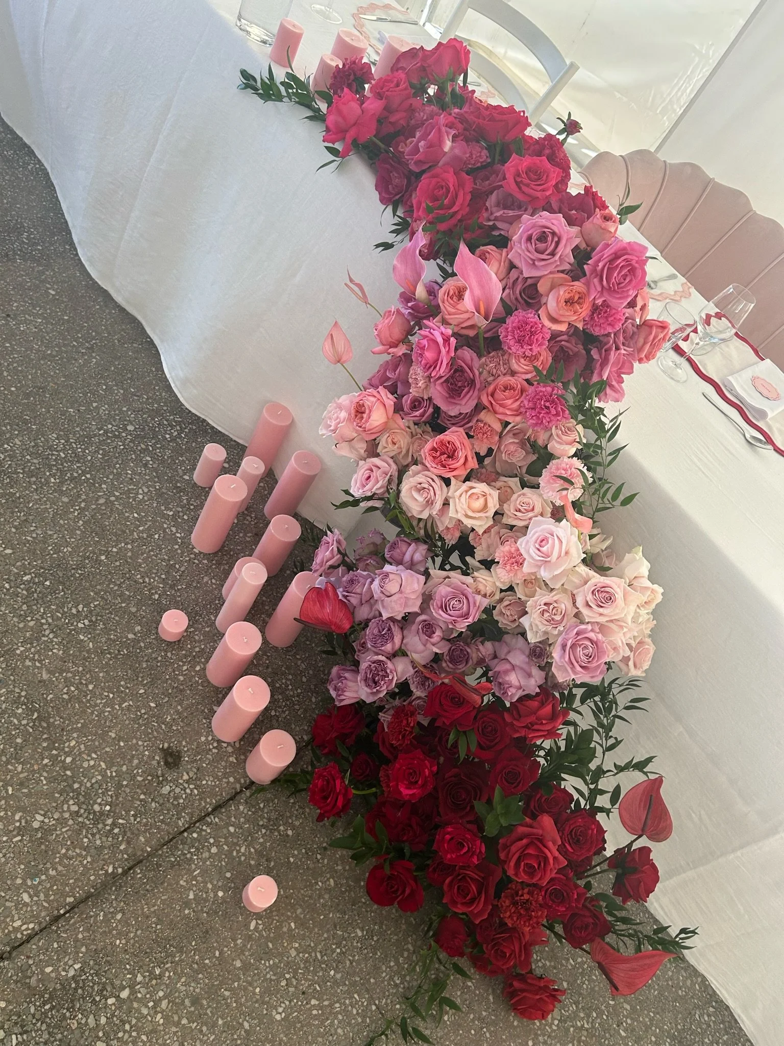 Table decorated with pink, lavender, and red roses, with pink candles on the floor.
