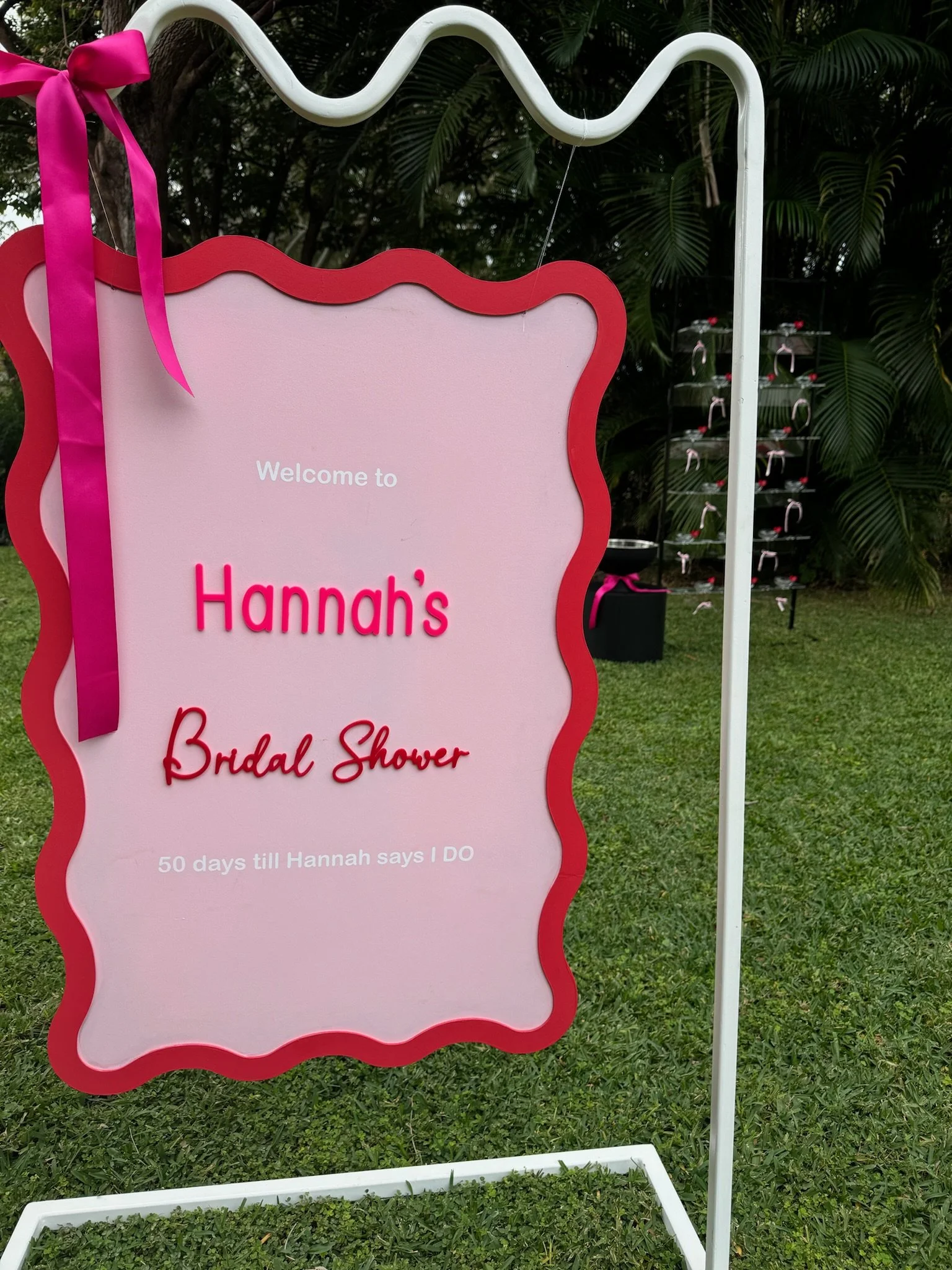 Pink and red bridal shower sign with a pink ribbon, welcoming guests to Hannah's bridal shower, with a countdown of 50 days until she says 'I do'.