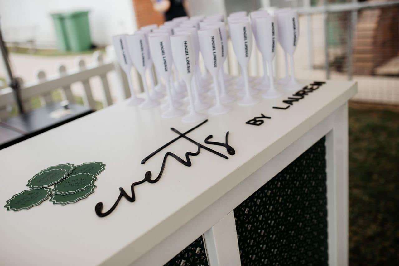 A white card with the name 'sweet treats' written in black cursive, and a small stack of green circular coasters. Several small plastic cups with white lids and black text are arranged on the card, labeled 'Margarita Lounge'.