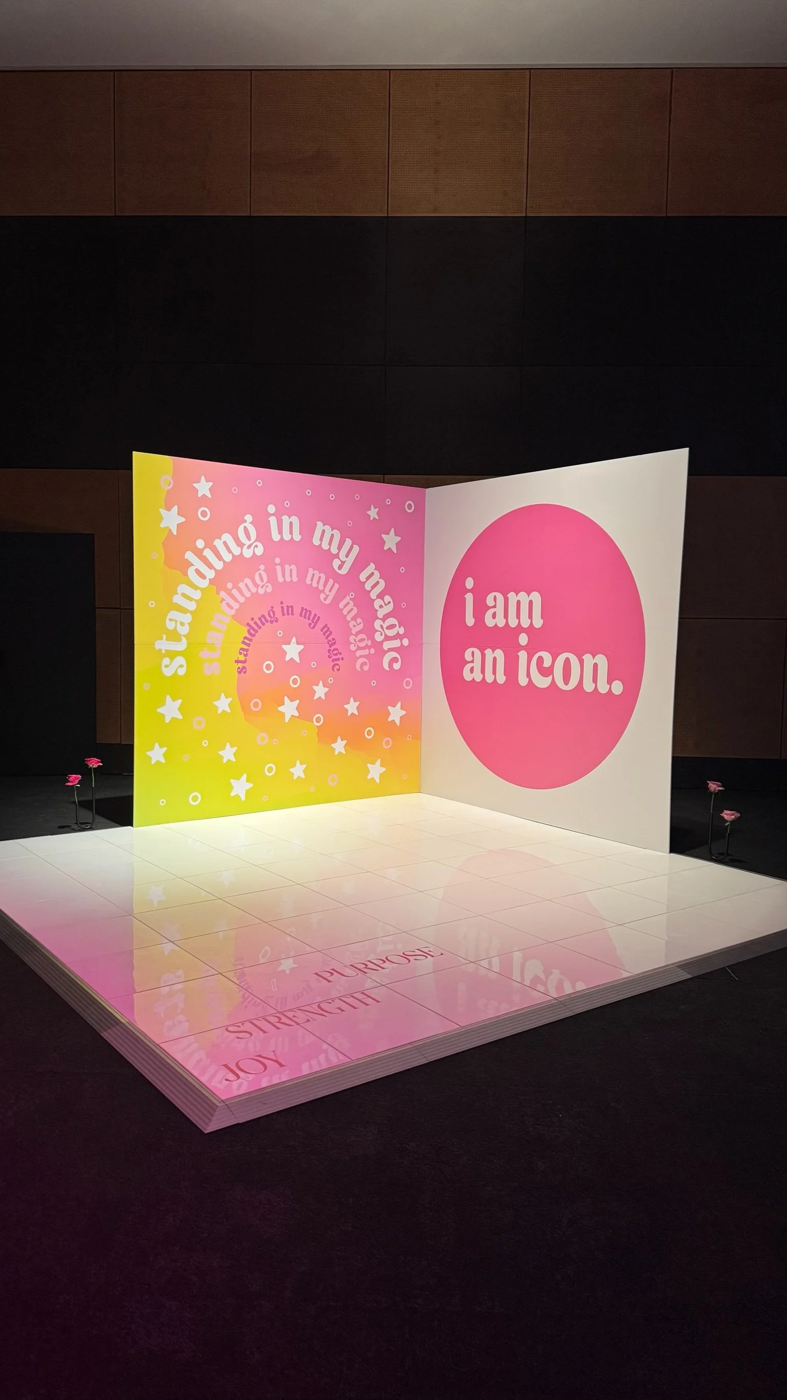 Colorful display with words 'standing in my magic' and 'I am an icon' on pink and yellow backgrounds, decorated with stars and circles, on a white platform.