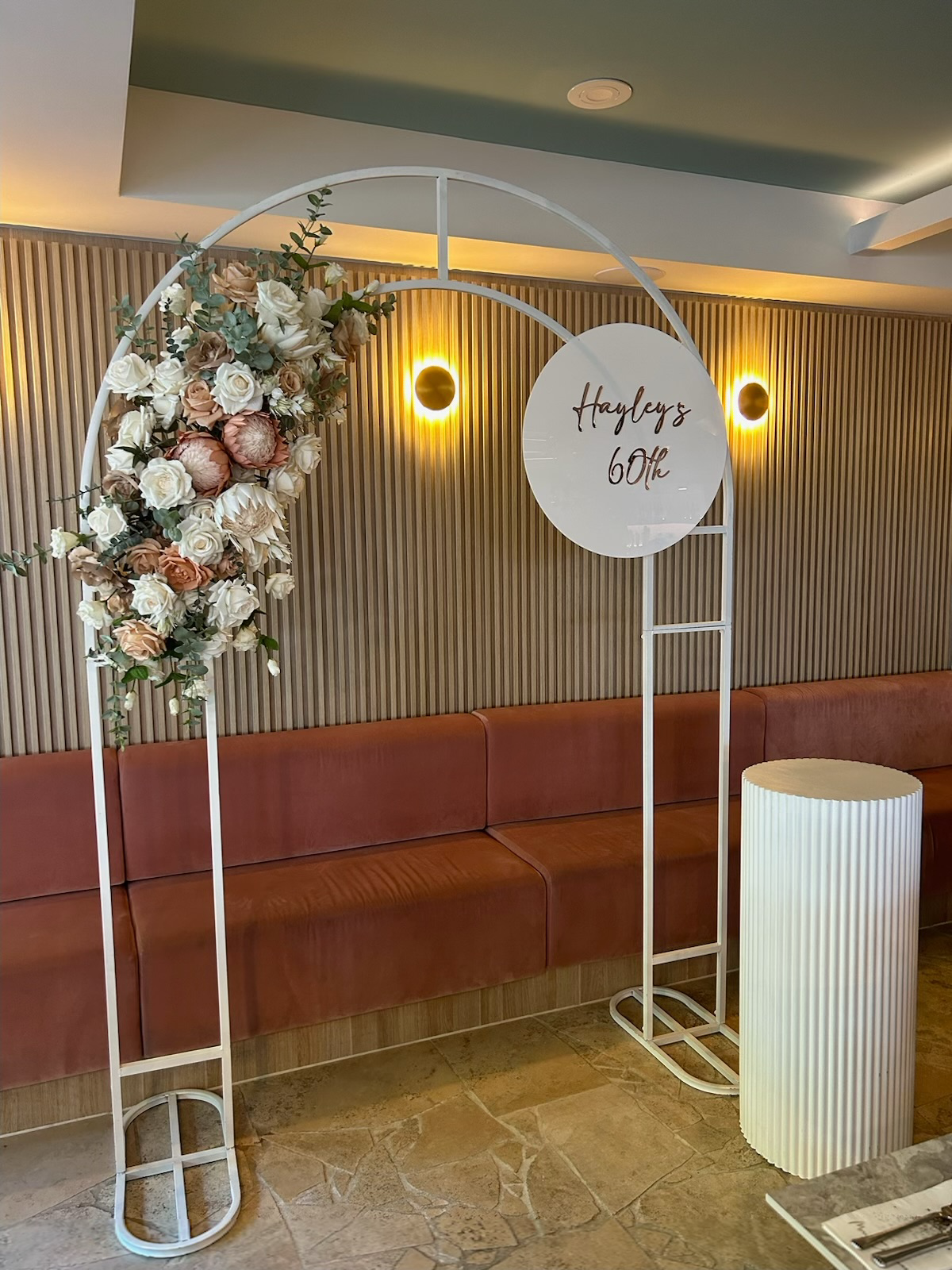 Decorative arch with floral arrangements and a sign reading "Hayley's 60th" in a decorated space.