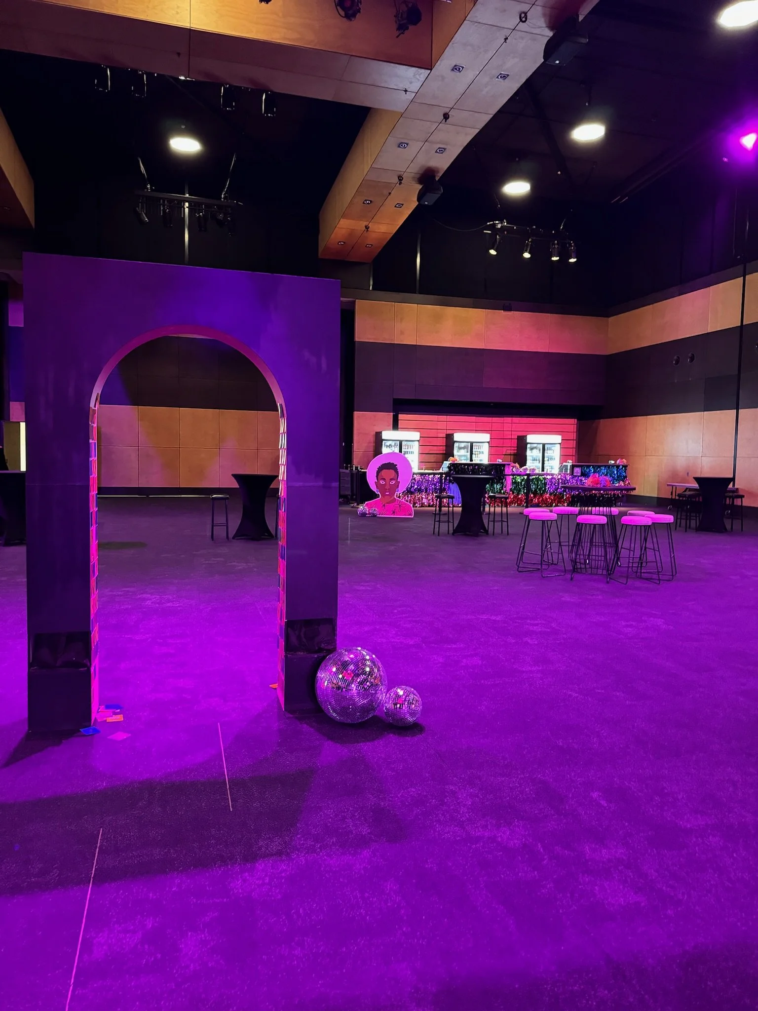 Event space with purple lighting, a large purple archway, disco balls on the floor, and a bar area with vending machines in the background.