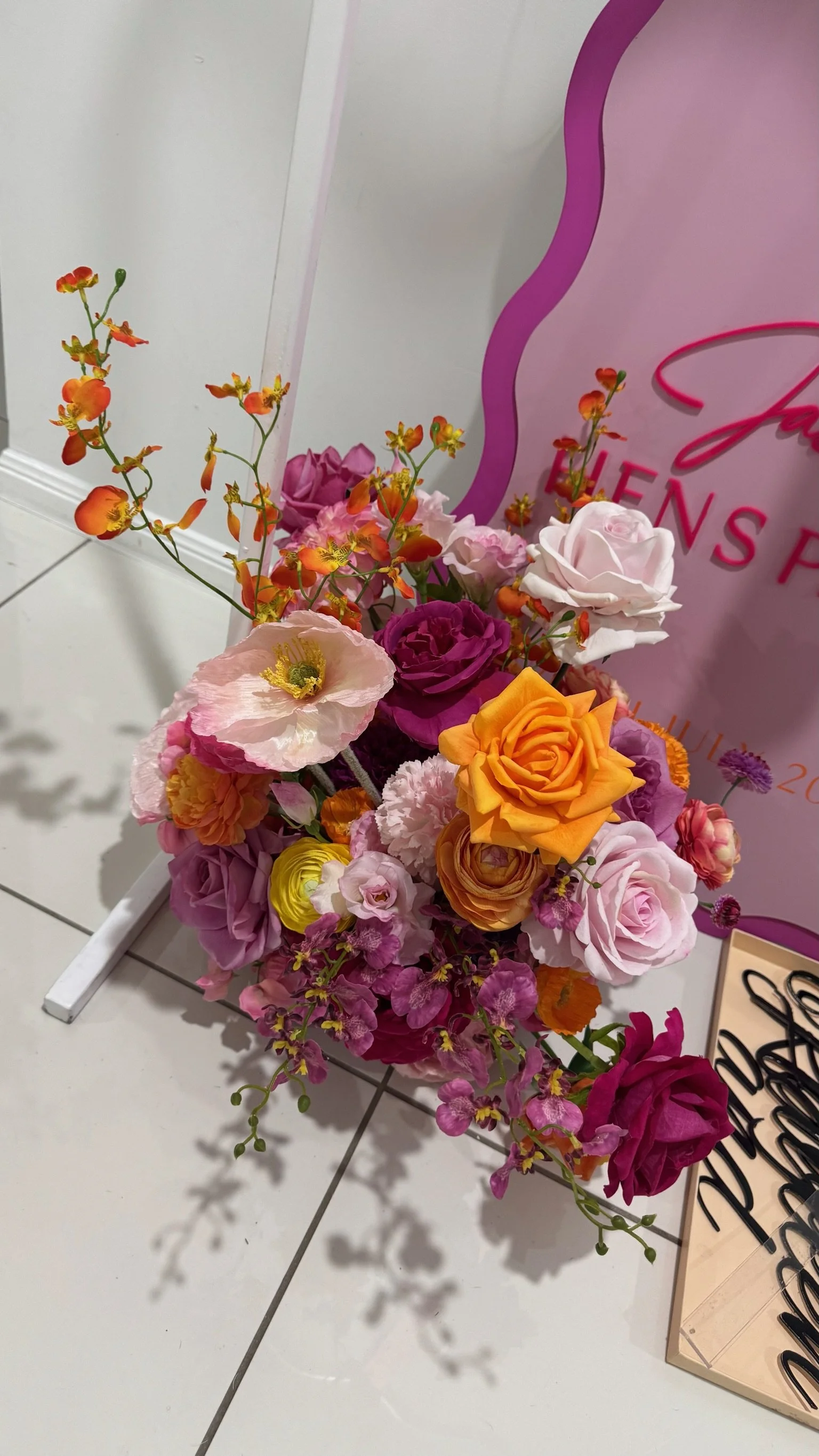 Colorful bouquet of various flowers including roses, poppies, and other small blossoms arranged beside a pink and purple promotional display.