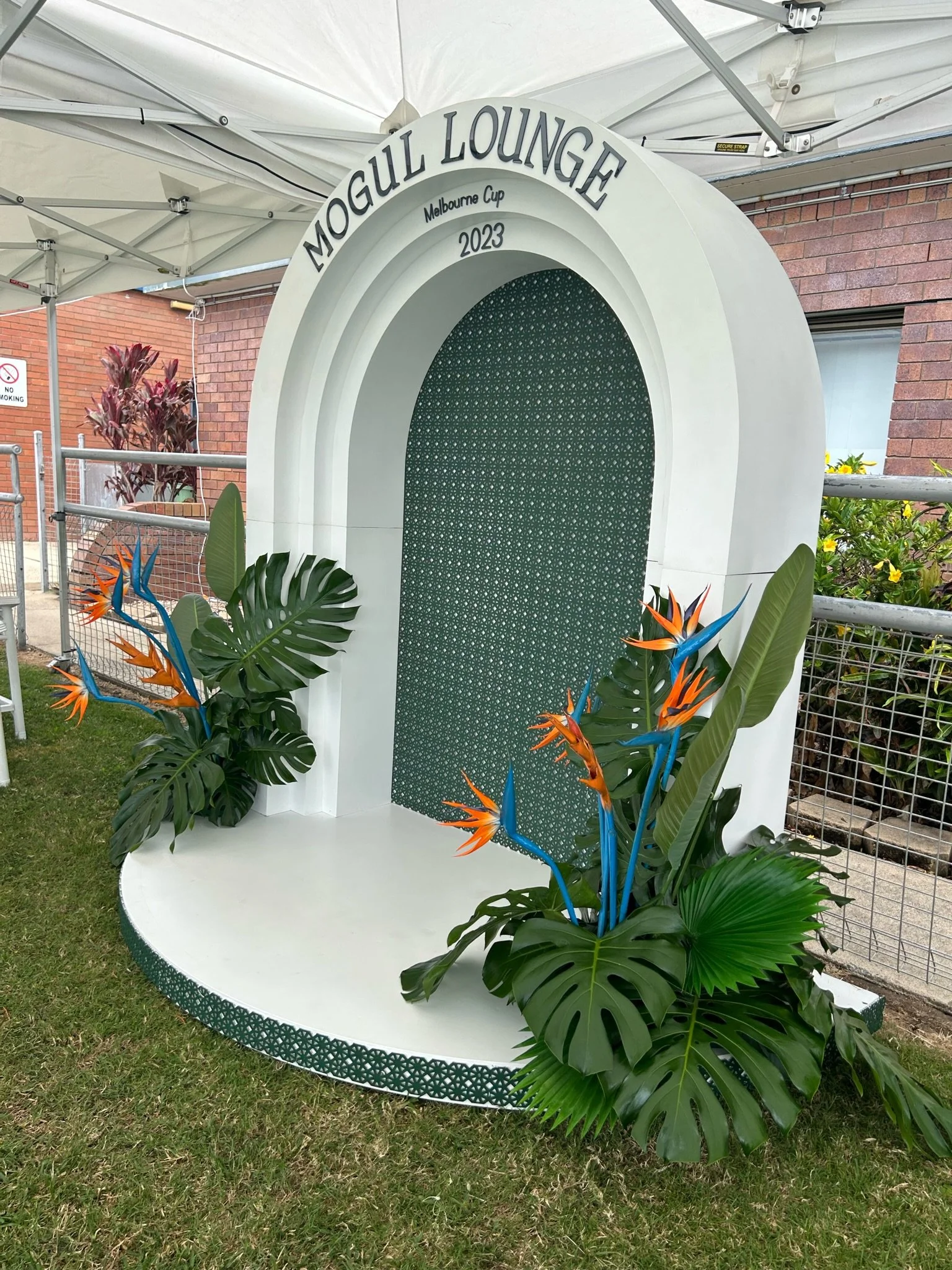 Decorative photo booth stand with tropical plants and flowers, labeled 'Mogul Lounge Melbourne Cup 2023'.