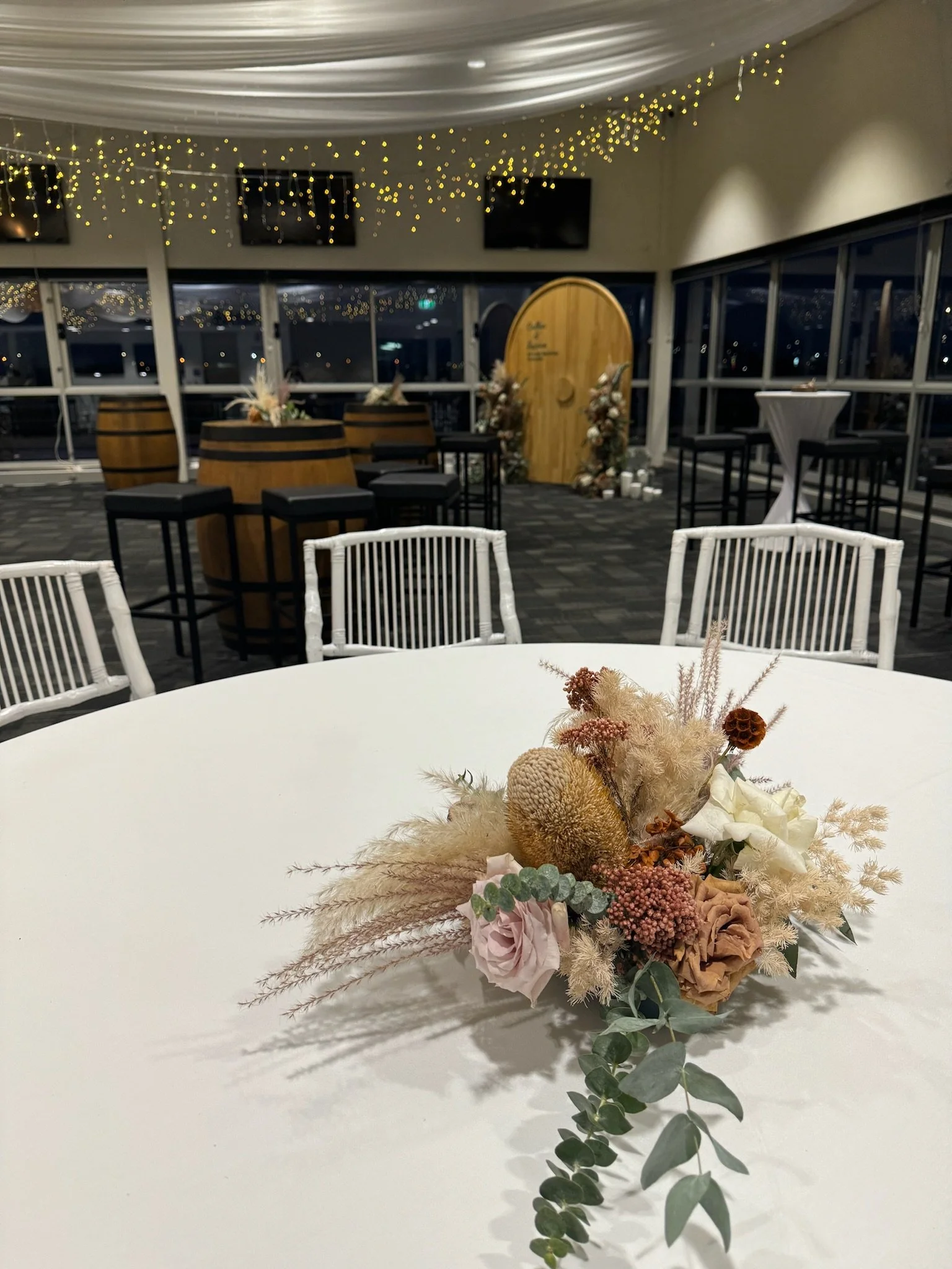 Elegant indoor event space decorated with fairy lights, featuring a table with a floral arrangement and a backdrop with floral decorations.