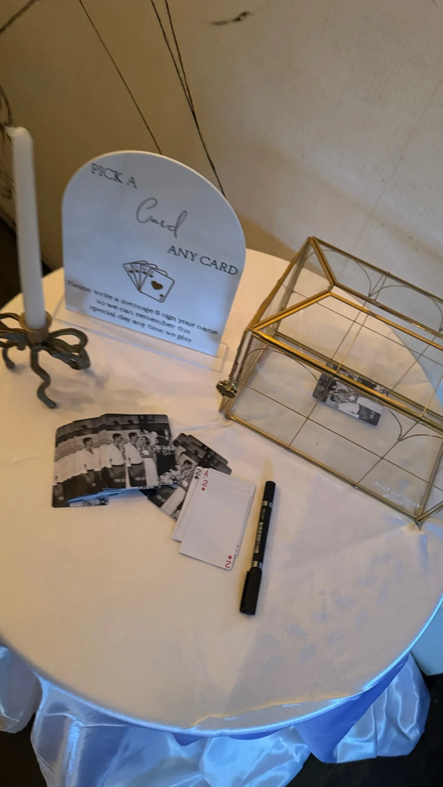 Table with a sign promoting a card game, a candle holder, photos of a group of people, playing cards, a black marker, and a glass display case.