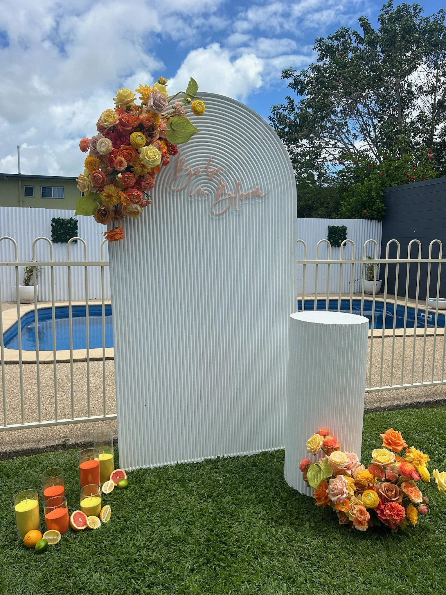 Decorative backyard scene with a white fence, pool, and floral arch with a 