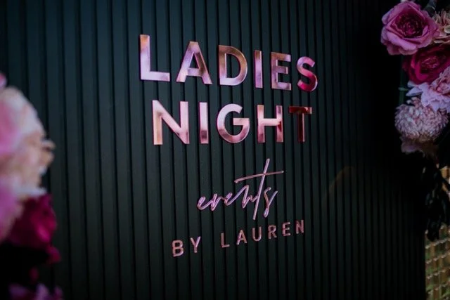 Decorative wall with pink text that reads "Ladies Night" and "events by Lauren," with pink flowers on the side.