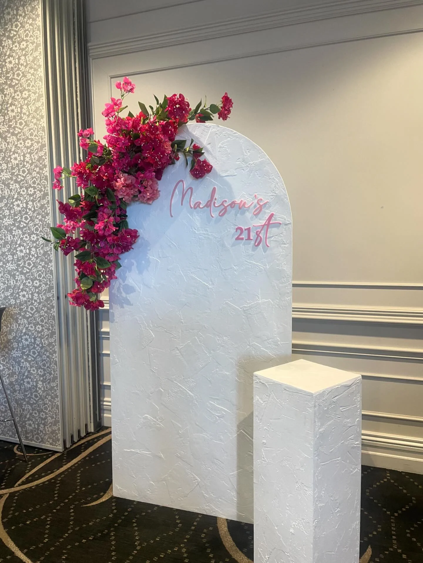 Wedding reception sign with pink flowers and the text 'Madison's 21st' on a white textured background.