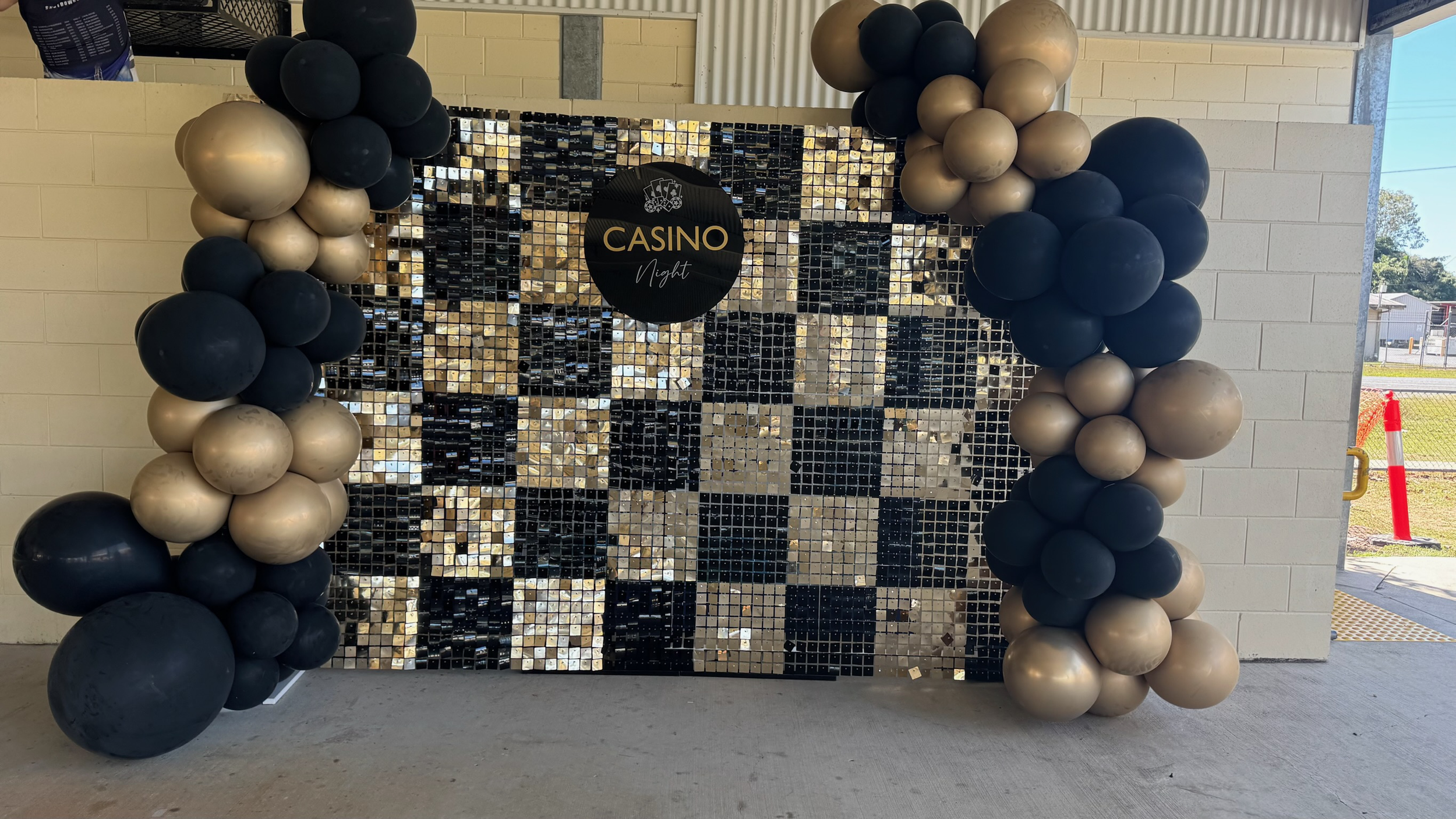 Decorative backdrop with black, gold, and dark gray balloons surrounding a mirror mosaic wall with a circular sign that reads "Casino Night".
