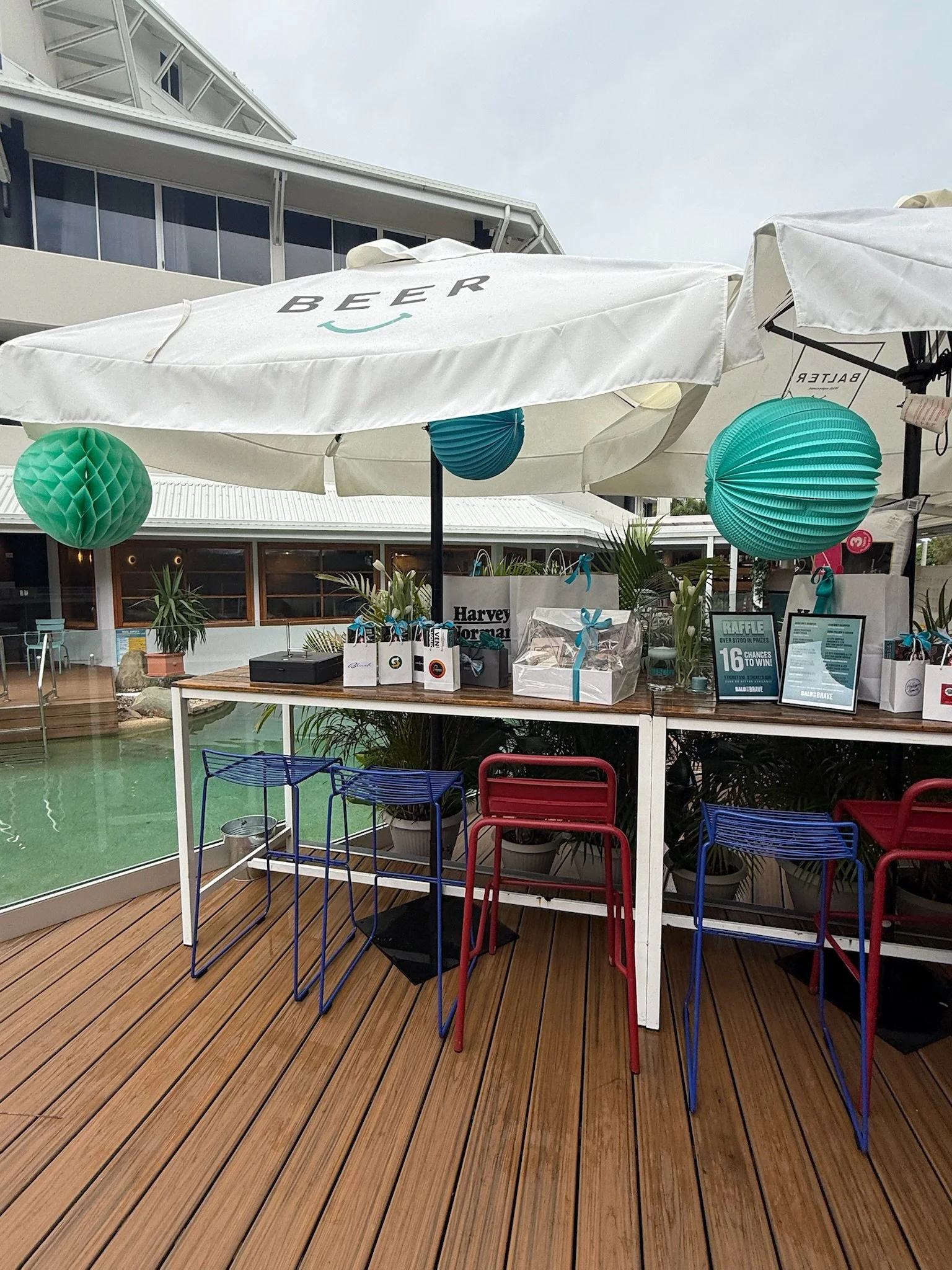 Outdoor bar area with umbrellas and hanging paper lanterns, set on a wooden deck with bar stools and potted plants.