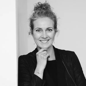 Sort-hvid portræt af en smilende kvinde med krøllet hår iført en sort jakke.