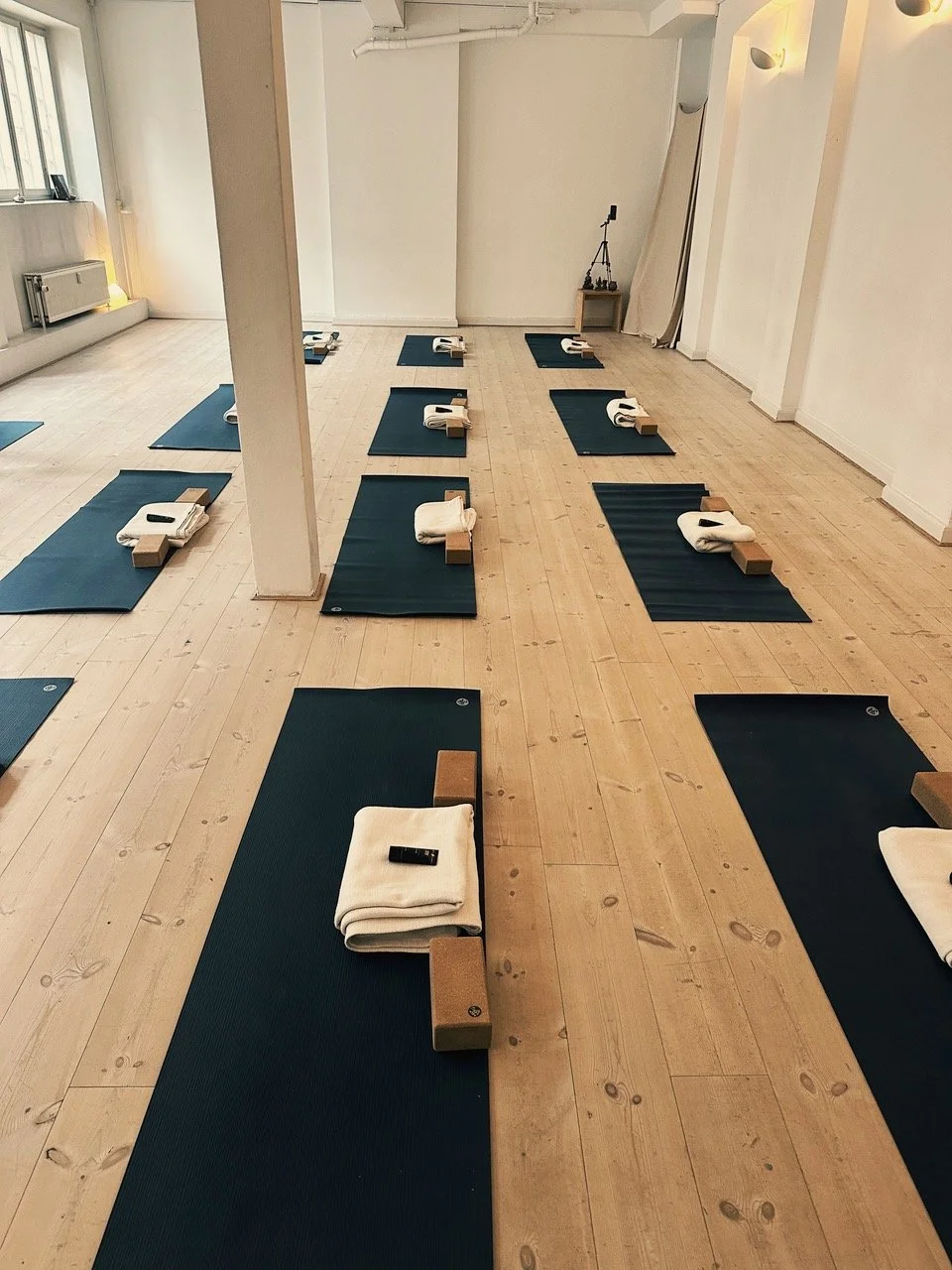 Et lyst yogastudie med sorte yogamåtter, træklodser, og håndklæder arrangeret på gulvet.