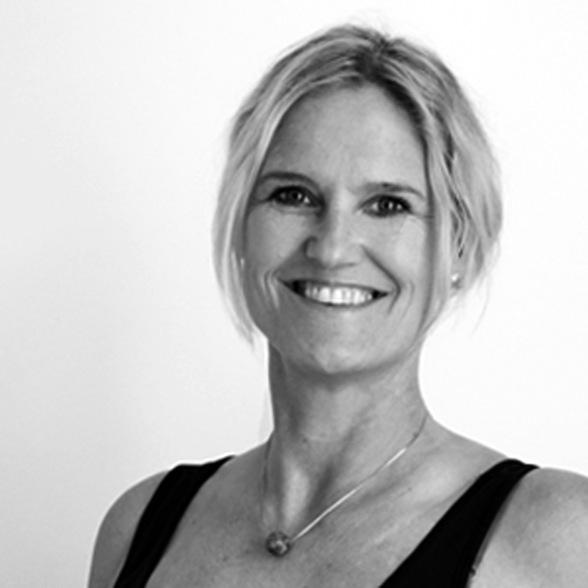 Sort-hvid portrætbillede af smilende kvinde med lyst hår og øreringe, iført en sort top.