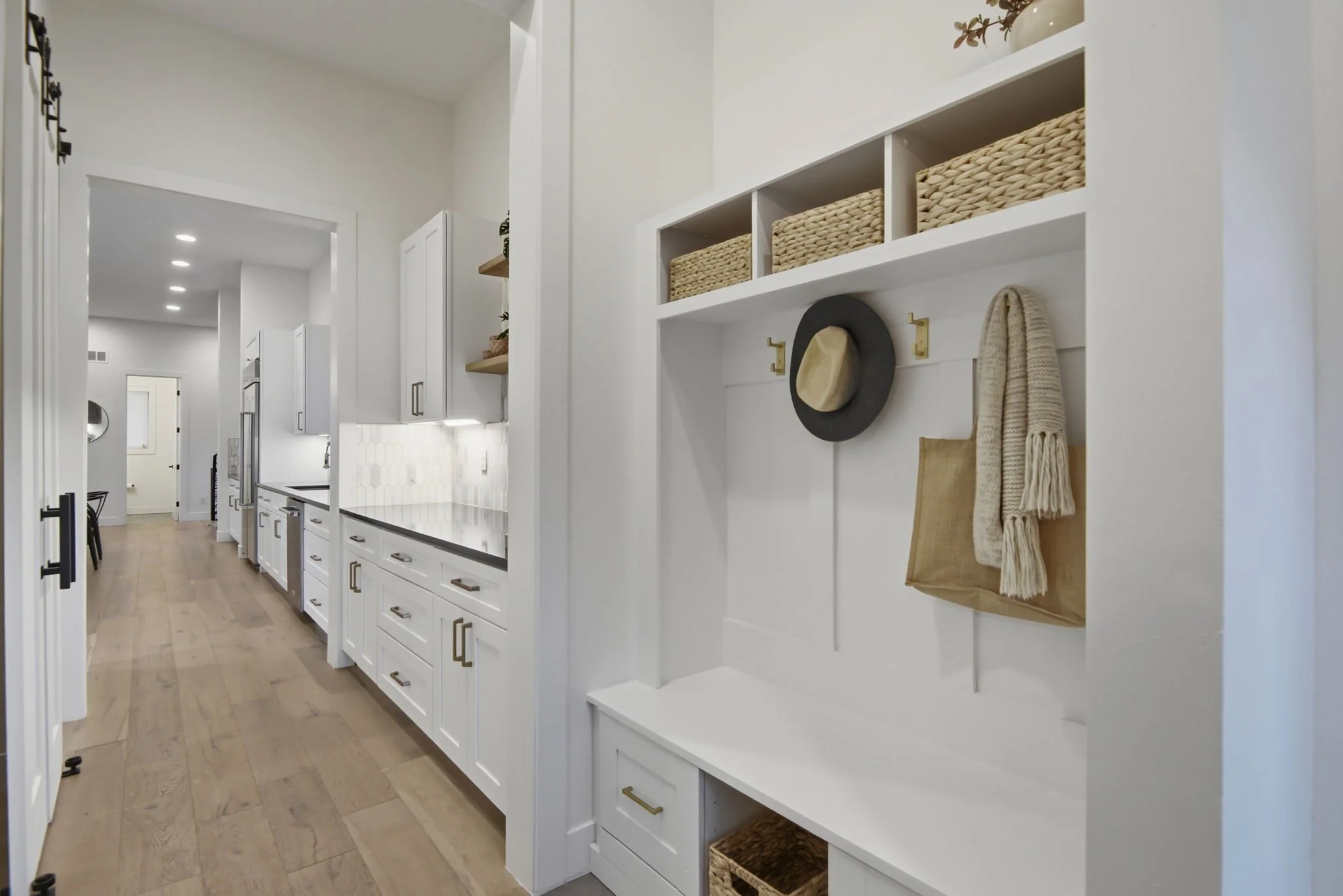 Interior of a modern kitchen with white cabinets, wooden flooring, and open shelving with woven baskets and accessories.