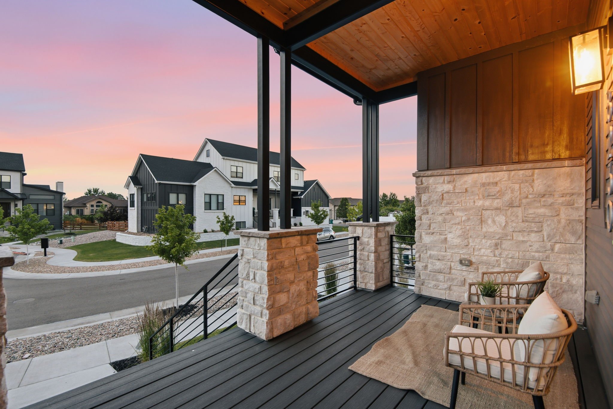 View from a porch showing a neighborhood with modern houses, trees, a sidewalk, and a colorful sky at dusk.
