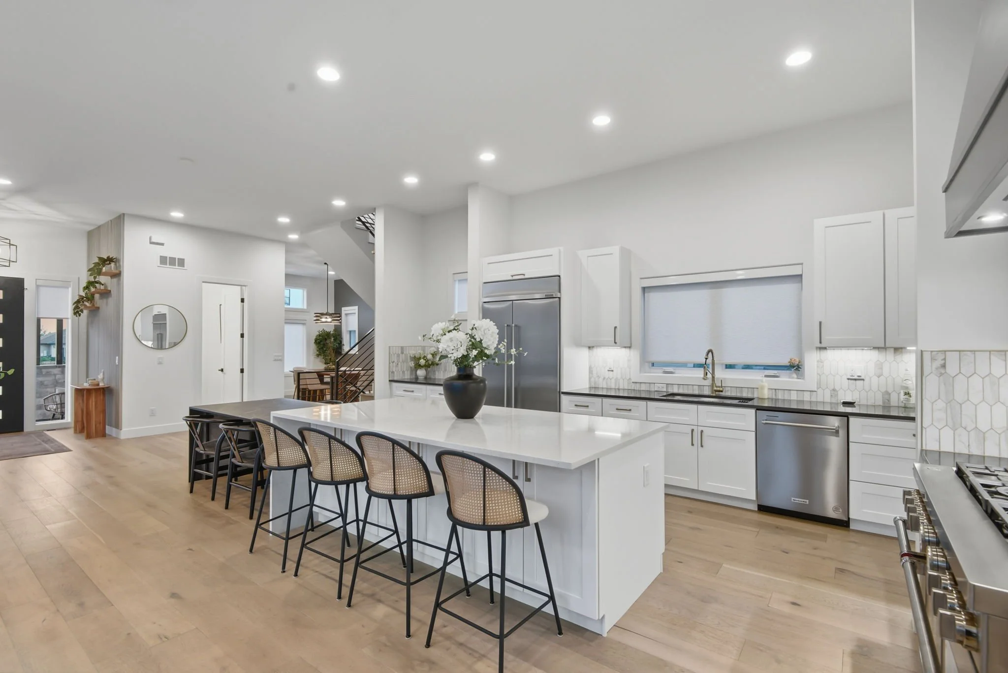 Modern kitchen with white cabinets, a large island with bar stools, stainless steel appliances, and a vase with white flowers.