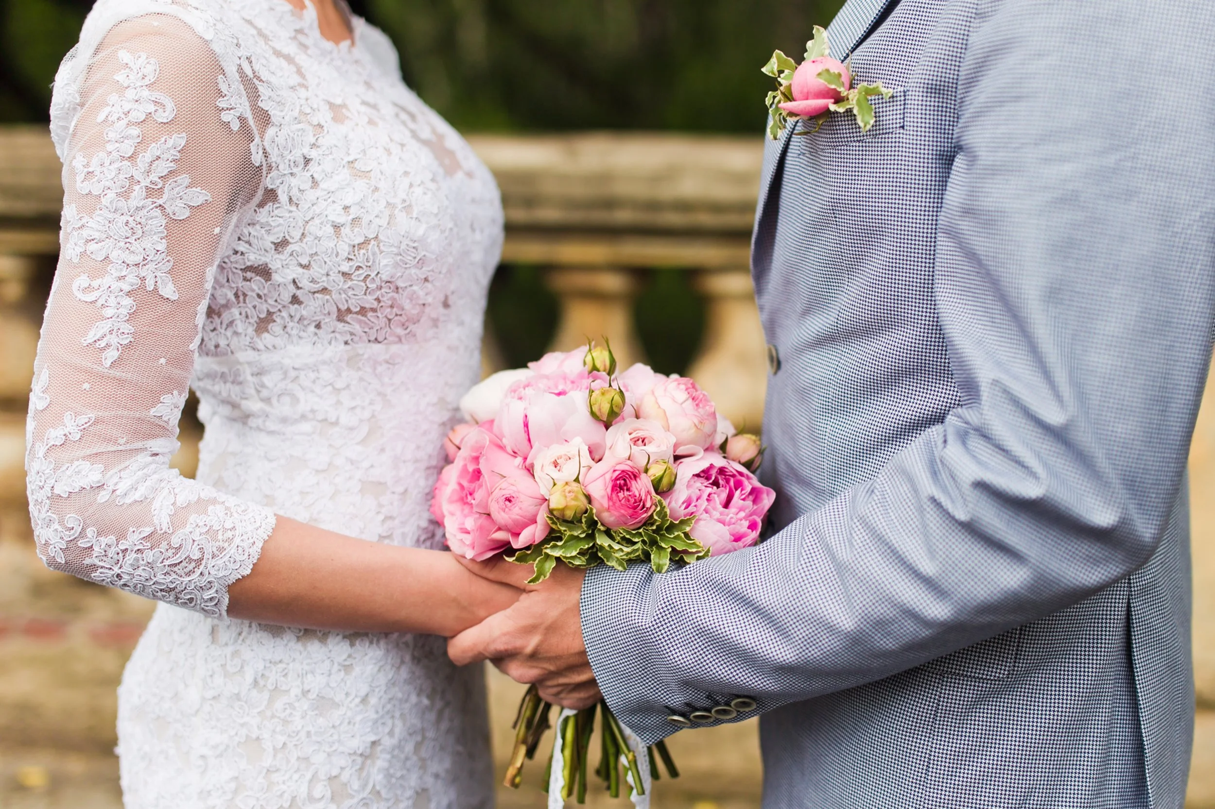 Ein Brautpaar bei der Hochzeit, die Hand des Mannes hält einen Blumenstrauß mit pinken und weißen Blumen.