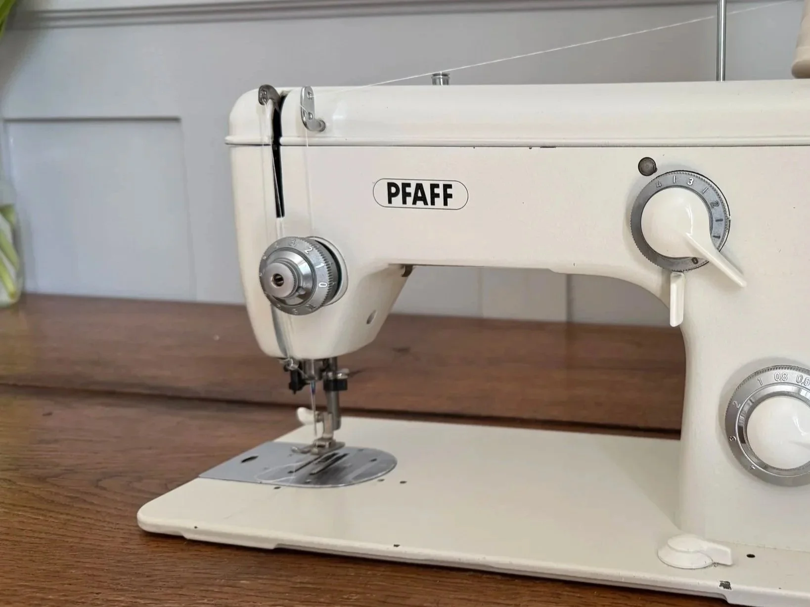 A cream-colored vintage Singer sewing machine on a wooden surface with a label that reads PFAFF on the front.