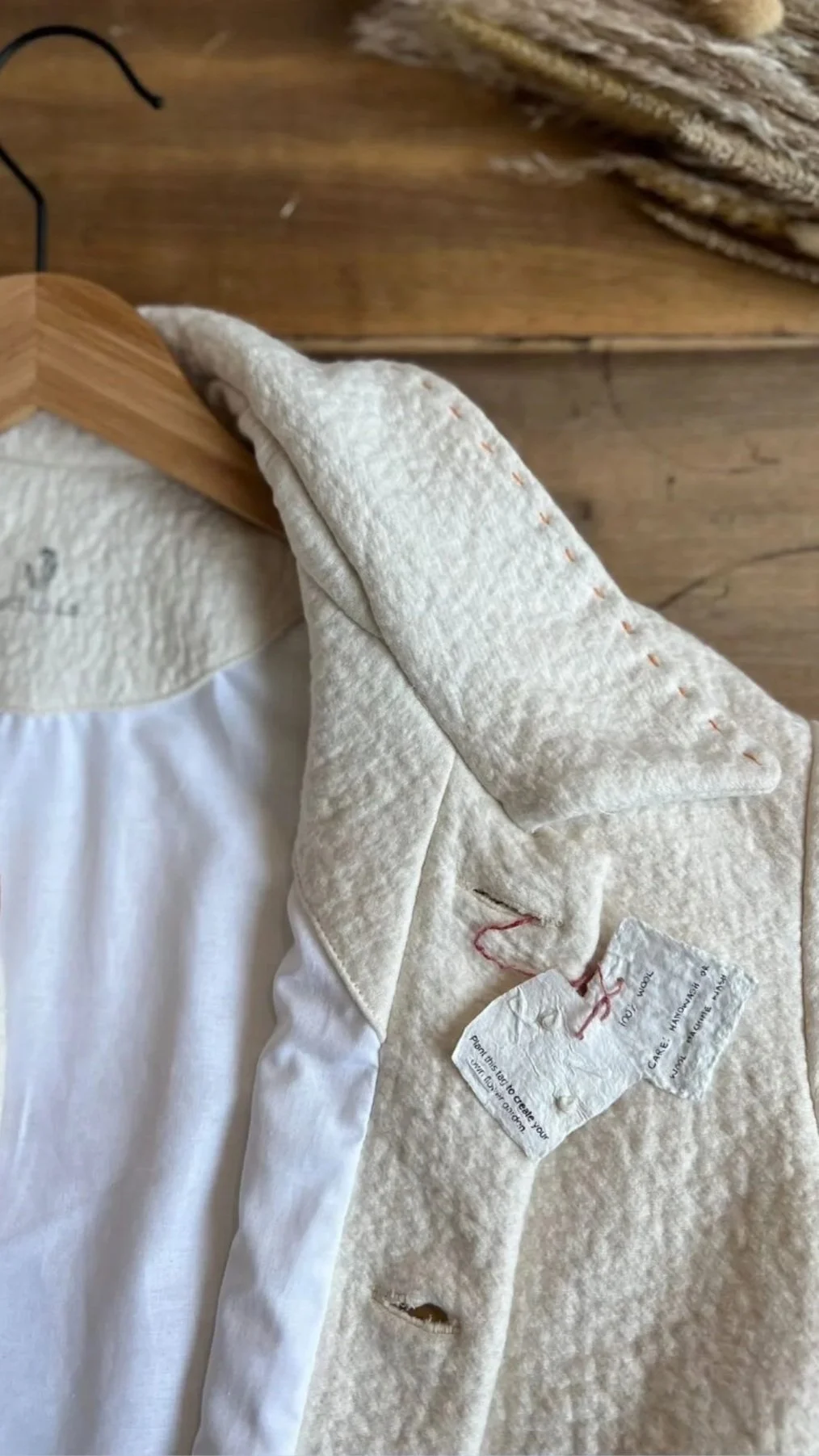 A white button-up coat hanging on a wooden hanger, with a tag attached. Cardamom The Label.