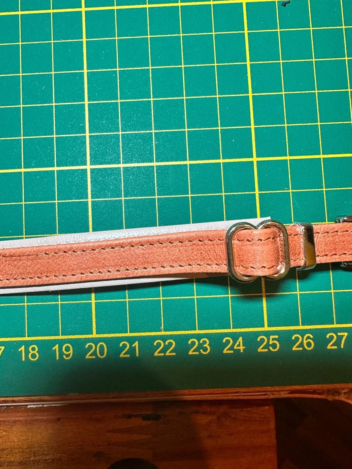 Cintura in pelle rosa su una superficie da lavoro da artigianato con una base a reticolo verde con linee gialle e numeri.