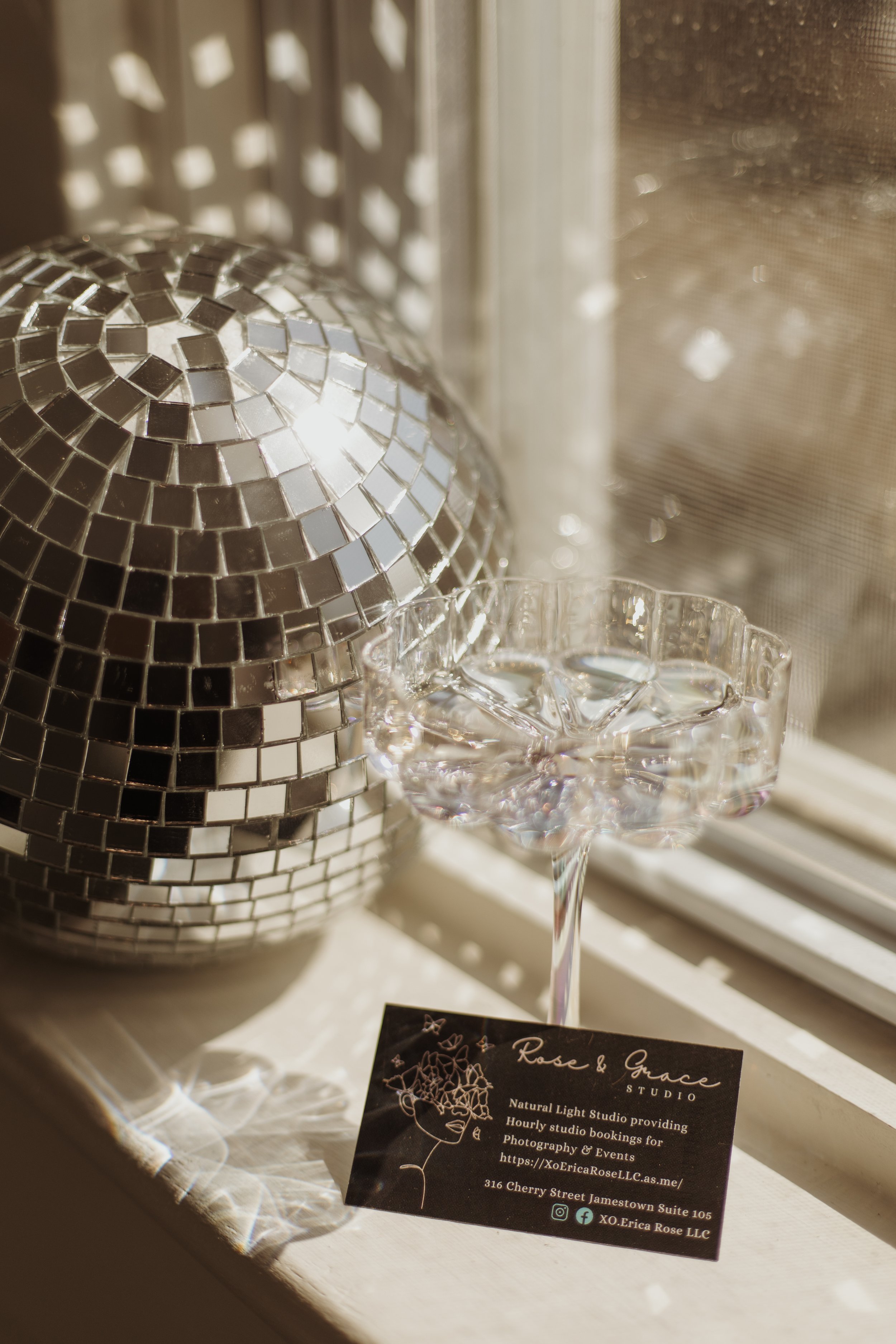 A decorative mosaic disco ball, a glass bowl with ice cubes, and a business card for Rose & Grace Studio on a windowsill.