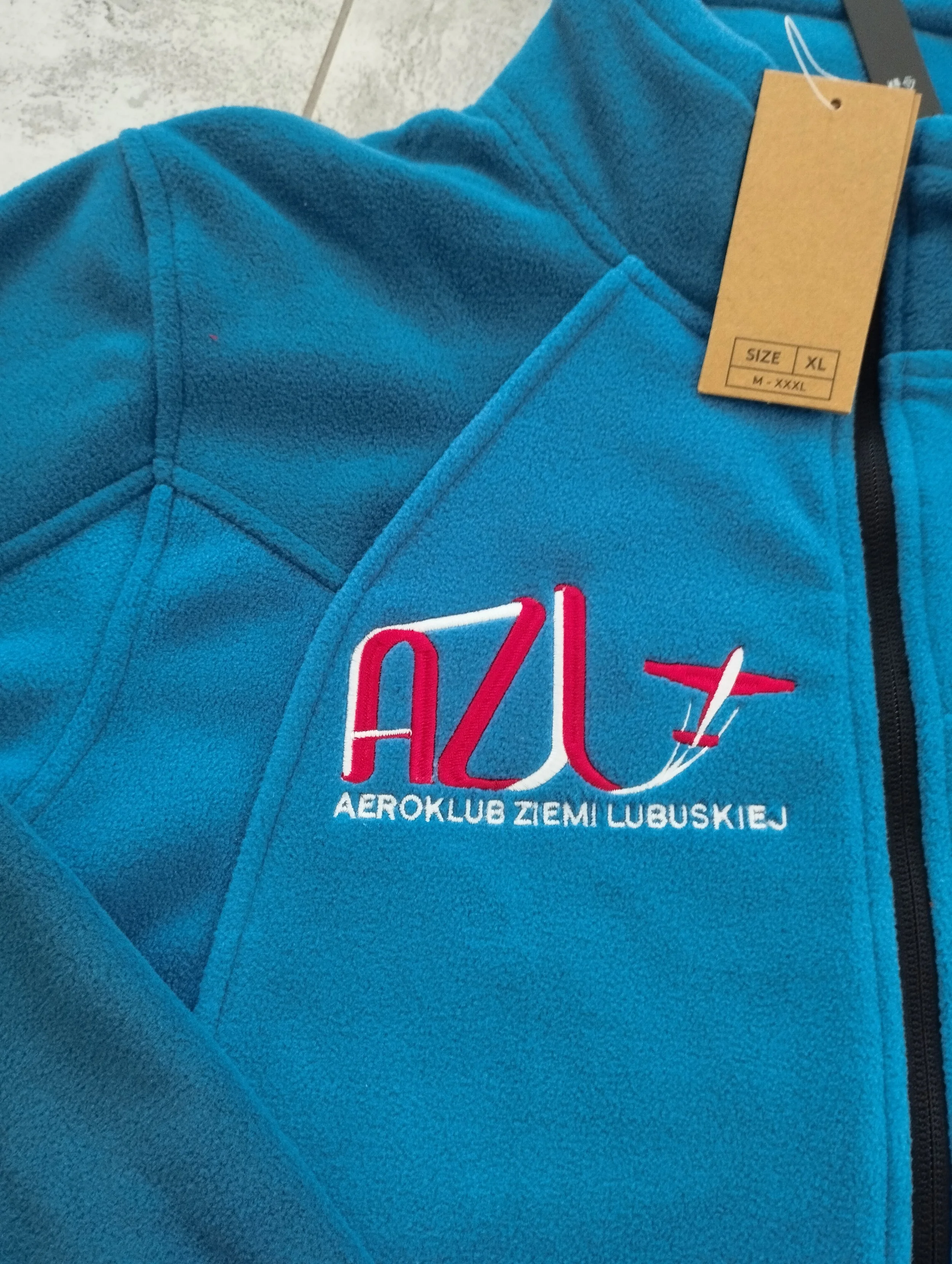 zdjęcie przedstawia niebieską bluzę polarową z napisem wyhaftowanym AZL