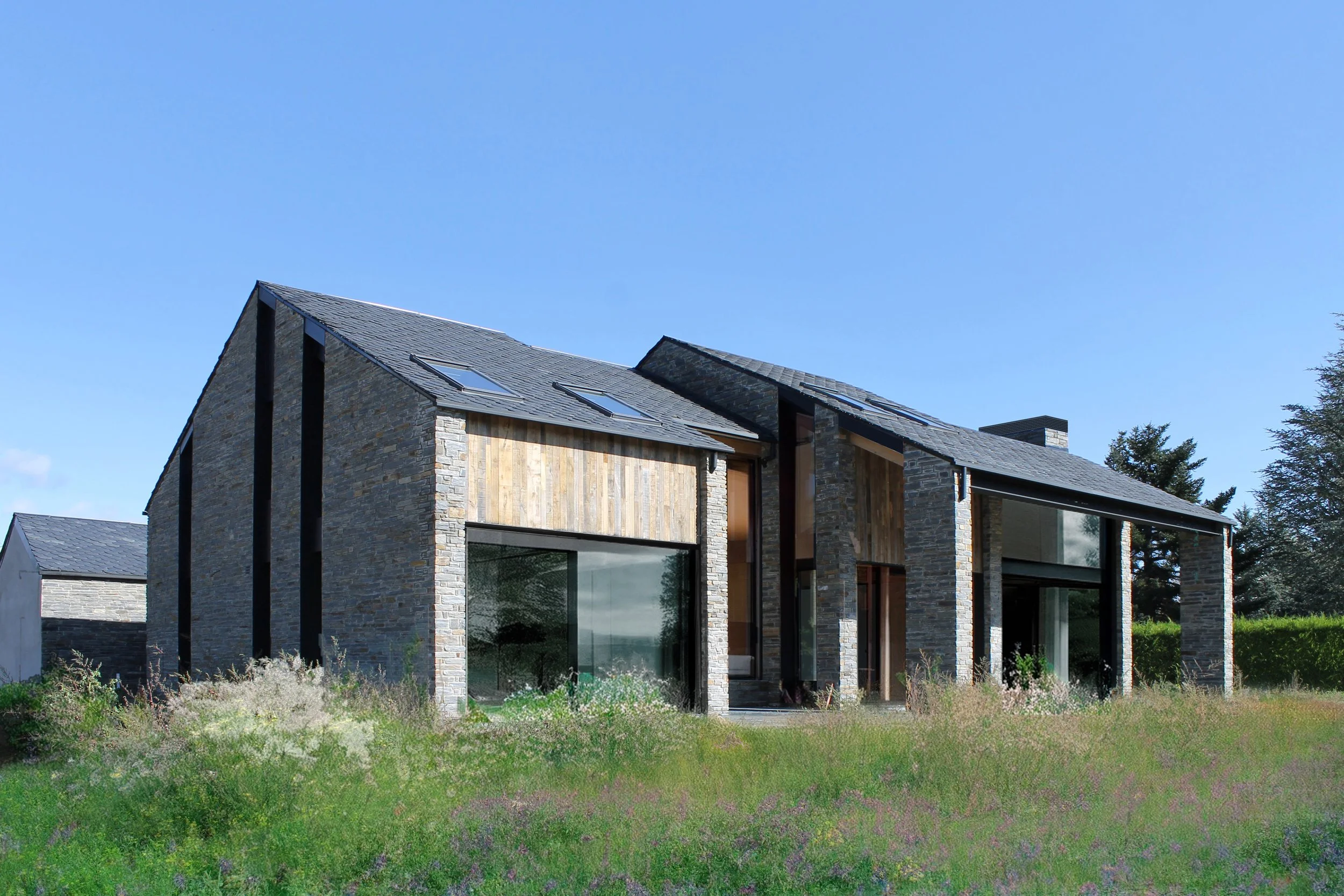Vivienda unifamiliar de arquitectura contemporánea con fachada de piedra y madera, grandes ventanales y cubierta inclinada.