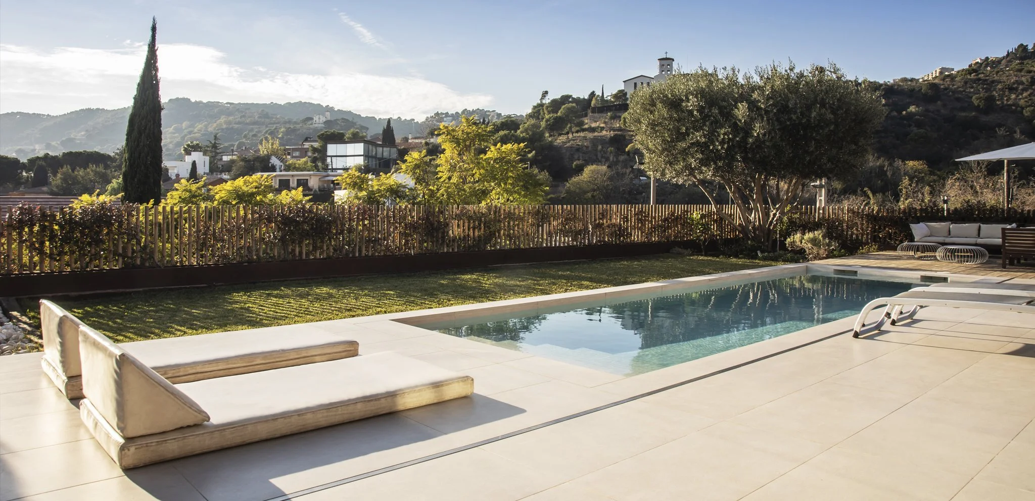 Piscina exterior con terraza, jardín y zona de descanso en una vivienda de arquitectura contemporánea con vistas al paisaje.